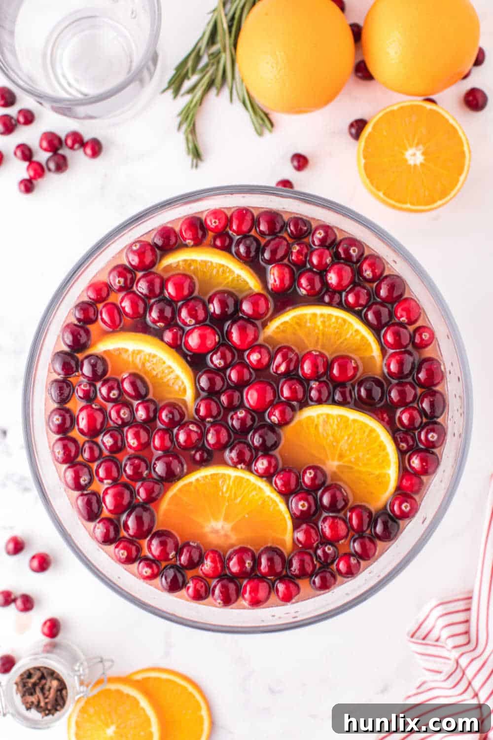 Crimson Spice Elixir 2 A beautiful Spiced Cranberry Punch in a large glass punch bowl, elegantly garnished with fresh cranberries, bright orange slices, and rustic cinnamon sticks. The punch bowl sits on a festive holiday table.