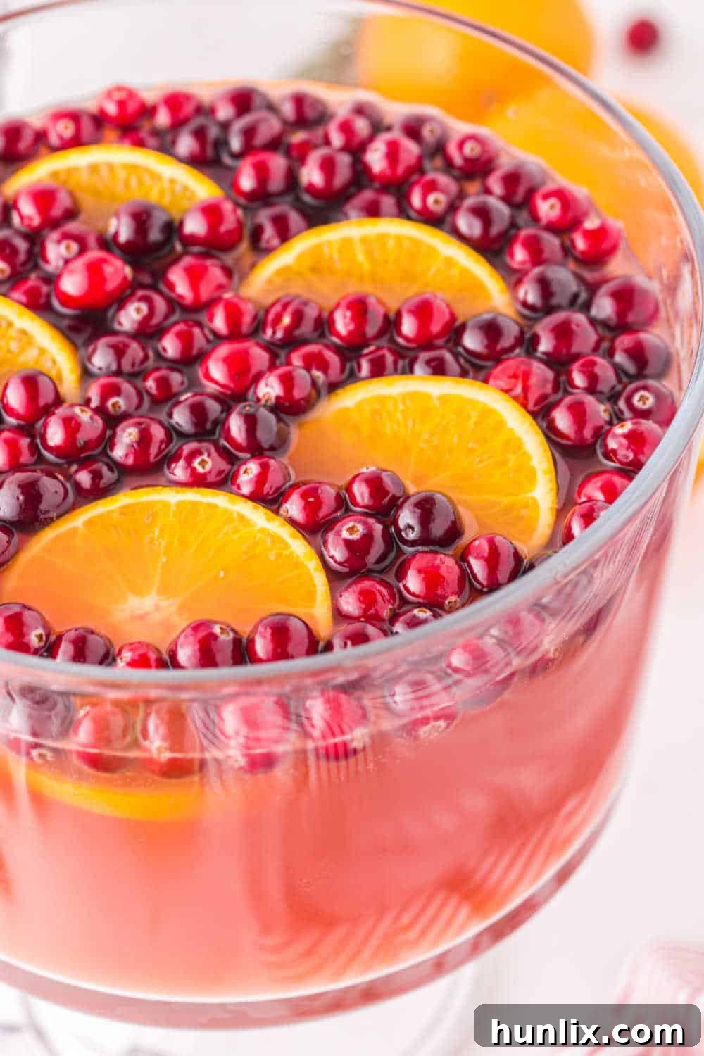 Crimson Spice Elixir 6 The vibrant Spiced Cranberry Punch beautifully presented in a large, elegant punch bowl, ready for guests to serve themselves. It is garnished generously with fresh cranberries, orange slices, and cinnamon sticks, sitting on a festive table setting.