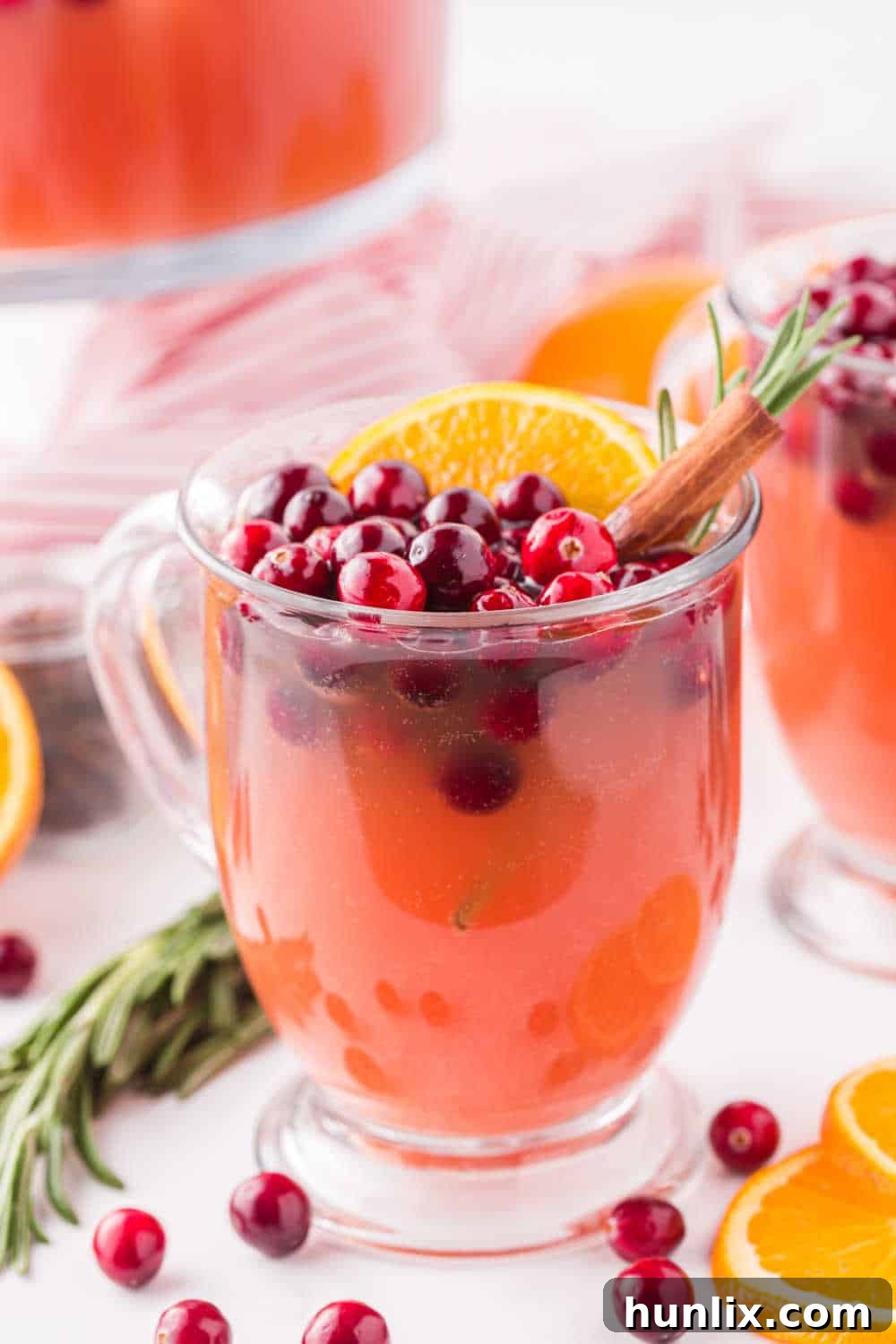 Crimson Spice Elixir 7 A single elegant glass of Spiced Cranberry Punch, artfully garnished with fresh red cranberries, a vibrant orange slice, and a slender cinnamon stick, positioned against a softly blurred festive background, ready for enjoyment.
