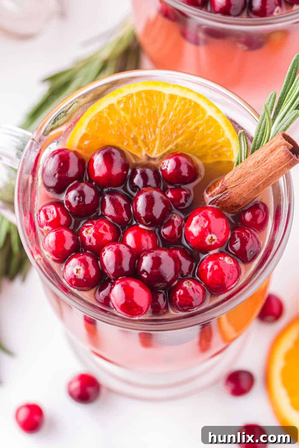 Crimson Spice Elixir 8 A close-up shot of Spiced Cranberry Punch in a clear glass, showing the rich red color, ice cubes, and festive garnishes like fresh cranberries and an orange slice, with a warm, inviting holiday background.