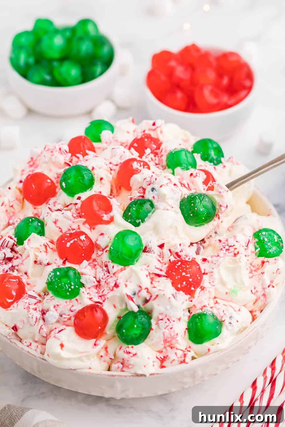 A serving bowl of Christmas Fluff with a spoon, highlighting its creamy, vibrant appearance and inviting texture, perfect for holiday enjoyment.