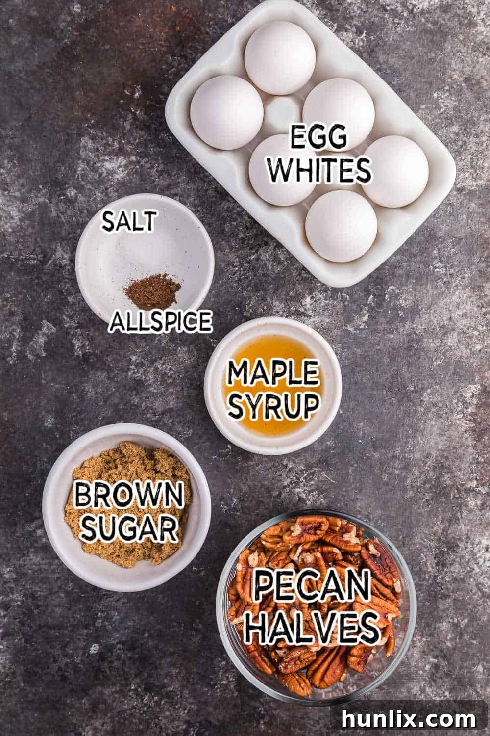 A selection of fresh ingredients, including pecans, brown sugar, maple syrup, and spices, laid out on a dark surface.