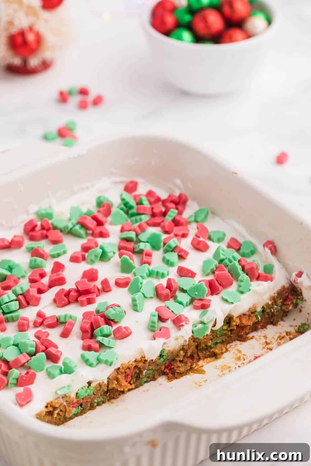 Christmas Chewy Bars in a white baking pan, with several pieces already cut out and ready to serve.