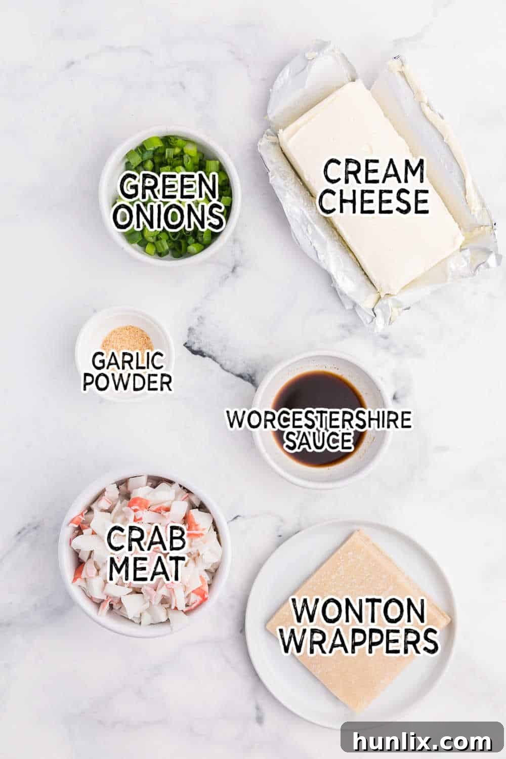 A flat lay of fresh ingredients laid out on a white marble counter, including crab meat, cream cheese block, sliced green onions, and a package of wonton wrappers.