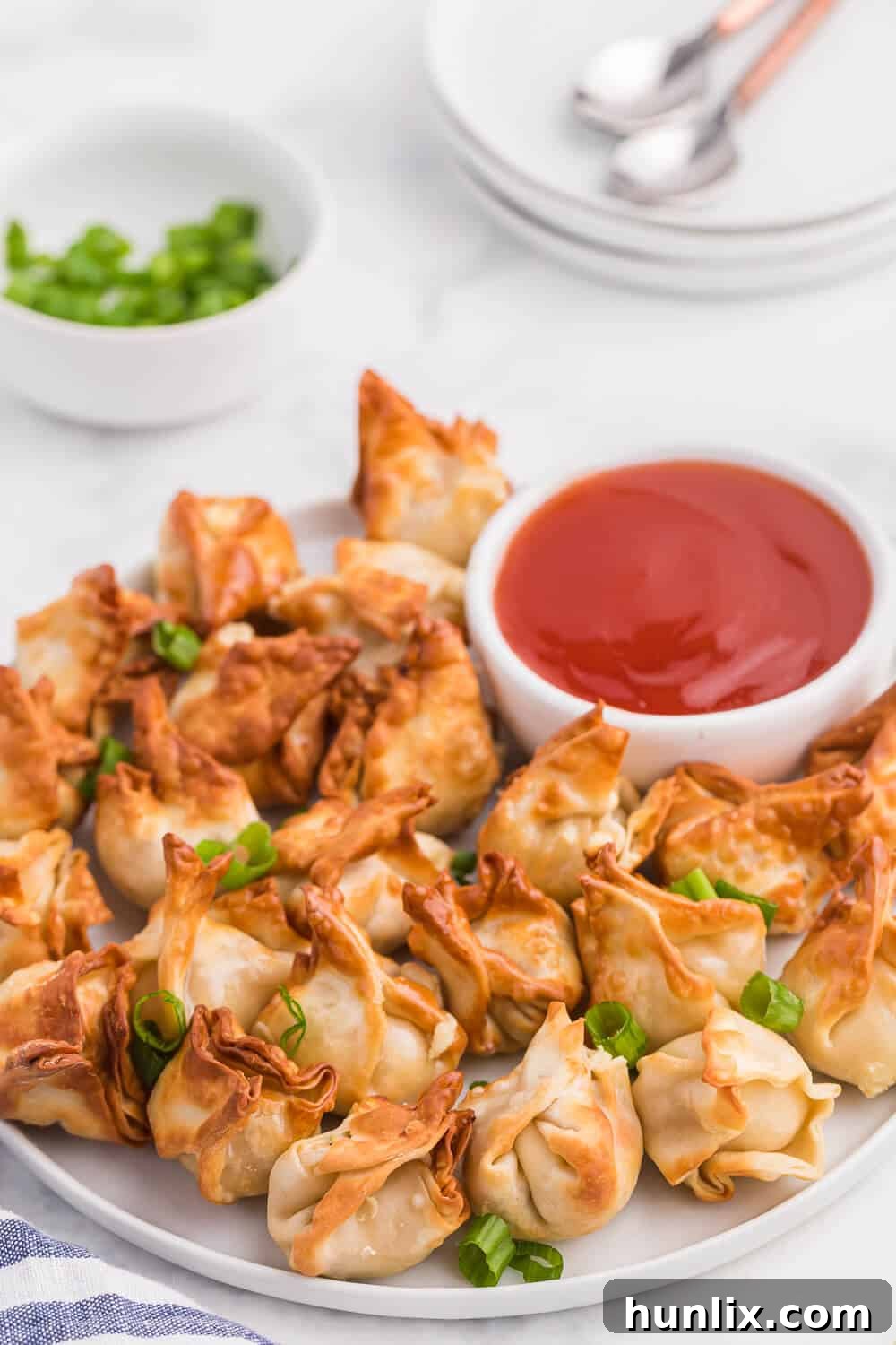 A beautifully arranged plate of golden air fryer crab rangoons, ready to be dipped into a small bowl of sweet and sour sauce.