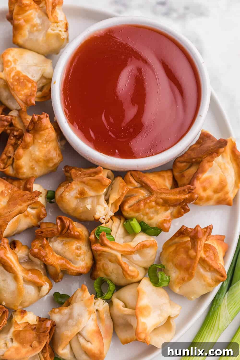 The crispy air fryer crab rangoons beautifully plated on a white dish, with a small bowl of sweet and sour sauce for dipping.