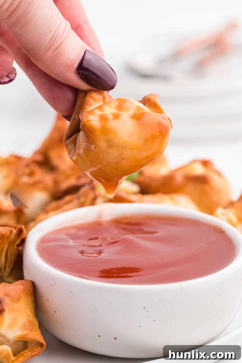 A hand reaching for a crispy air fryer crab rangoon, dipping it into sweet and sour sauce.