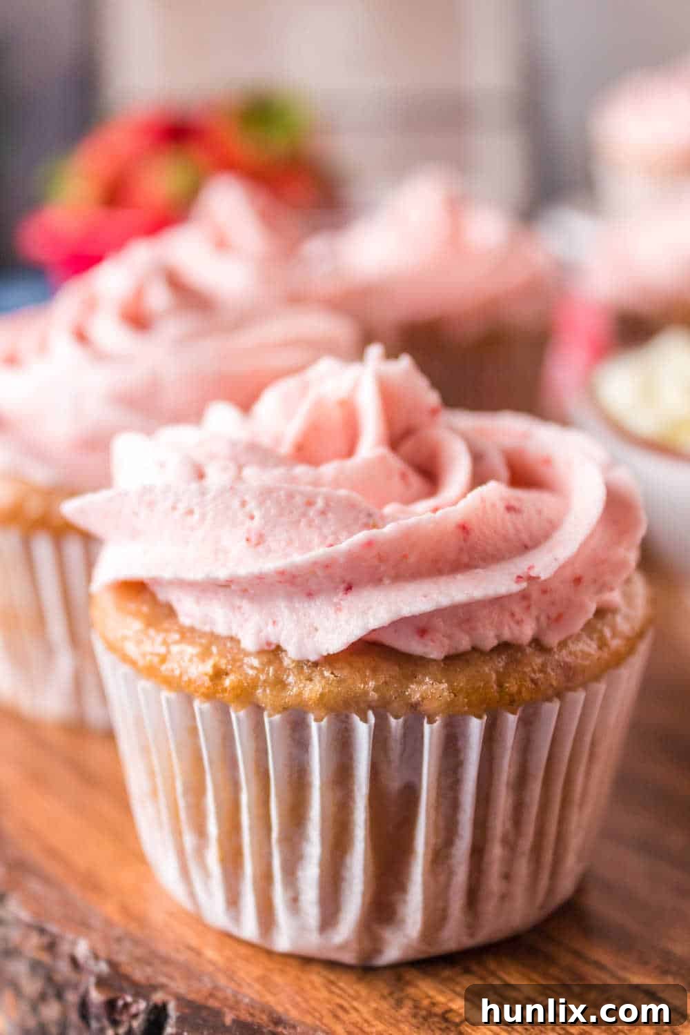 A single strawberry cupcake, beautifully frosted, resting on a rustic wooden platter.