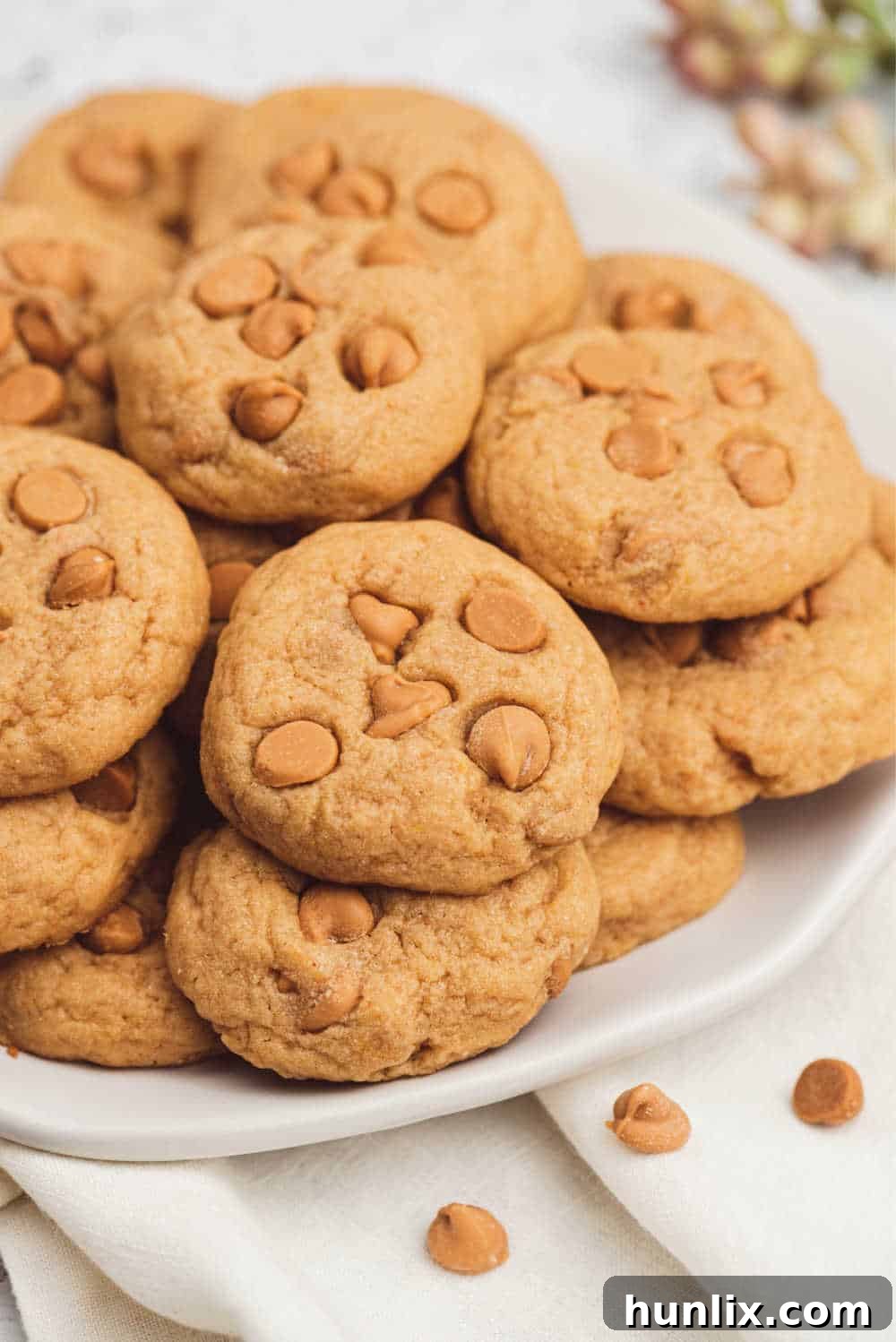 A stack of three butterscotch pudding cookies on a plate, highlighting their height and the visible butterscotch chips.
