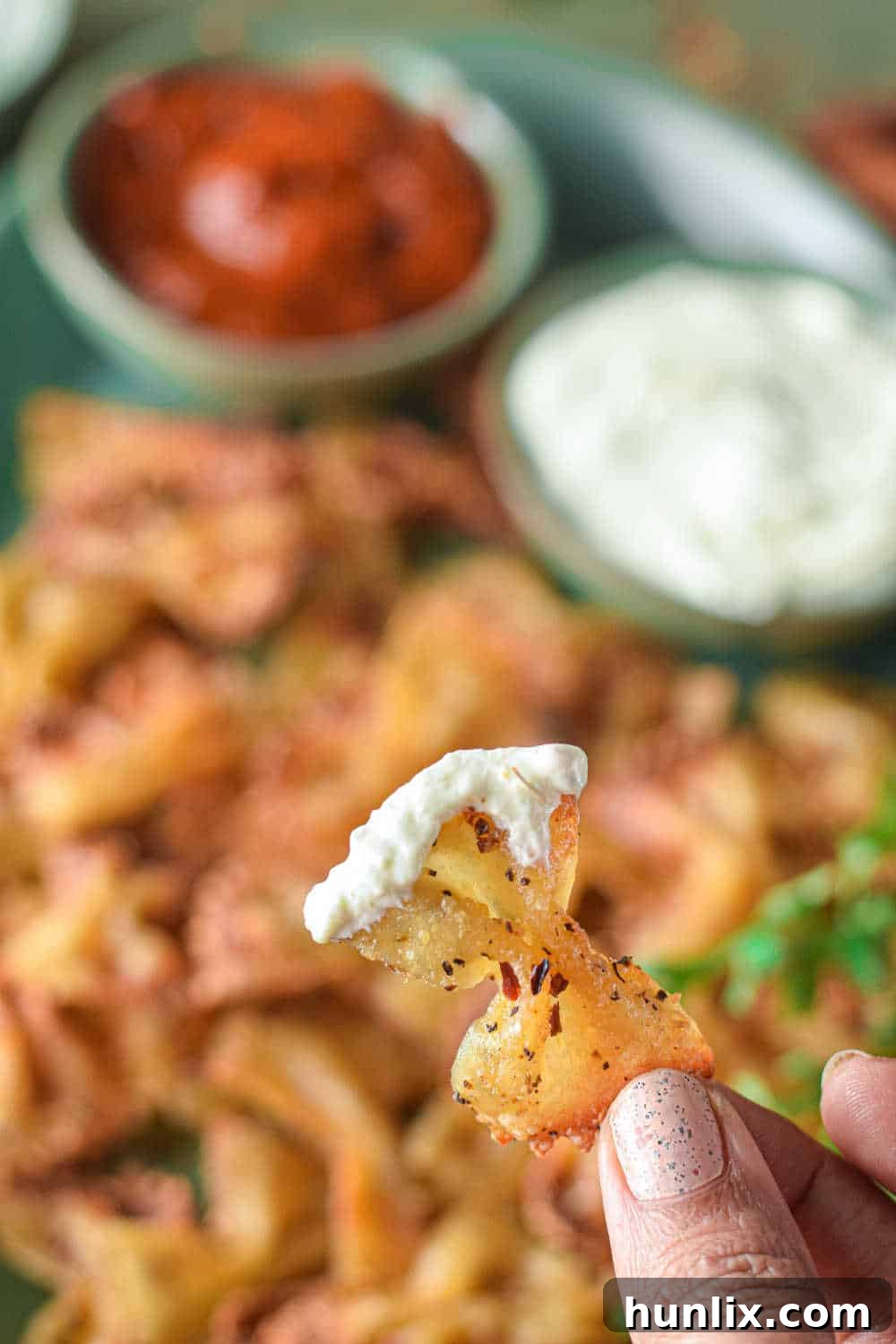 Air Fried Pasta Crisps 10 A hand holding a single air fryer pasta chip with a dollop of feta dip on it, ready to be eaten.
