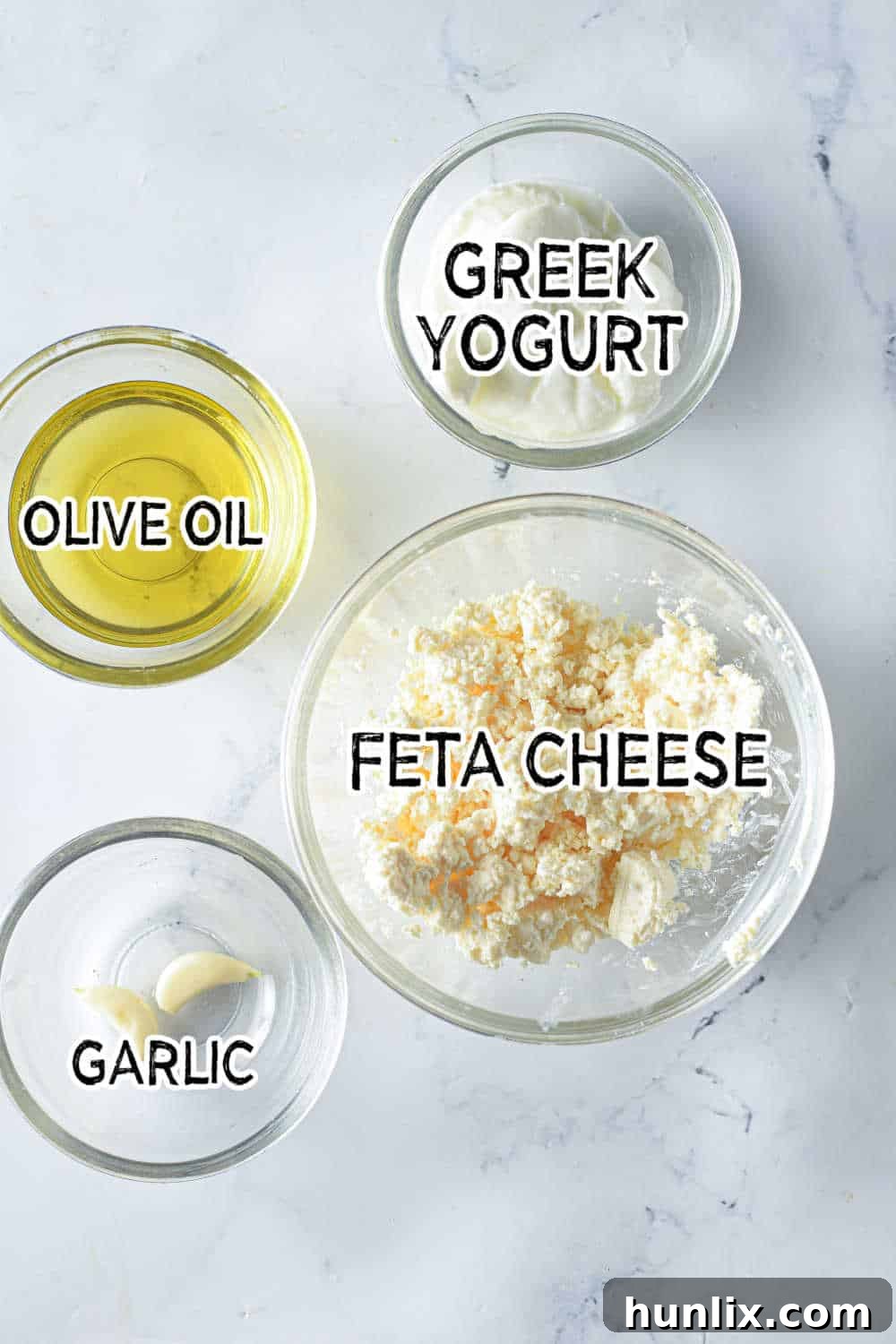 Air Fried Pasta Crisps 4 Ingredients for creamy feta dip arranged on a marble counter, featuring crumbled feta, Greek yogurt, garlic cloves, and olive oil.