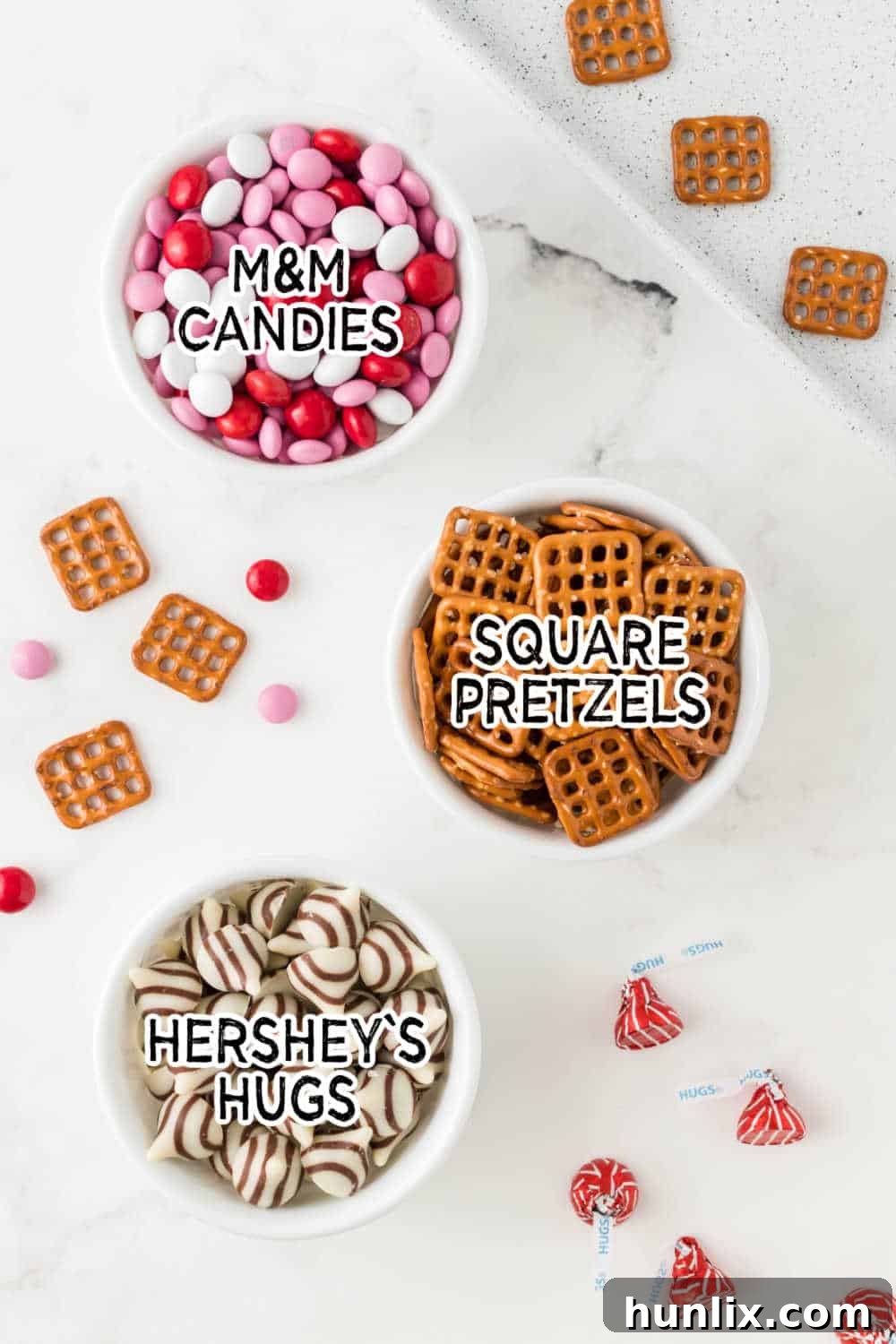 Three simple ingredients: Hershey's Hugs, M&M candies, and square pretzels, laid out on a marble background.