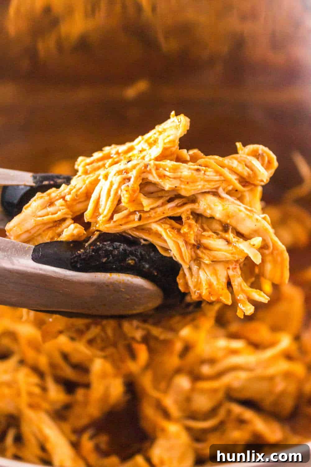 Tongs holding succulent Instant Pot BBQ shredded chicken, showcasing its tender texture and rich sauce.