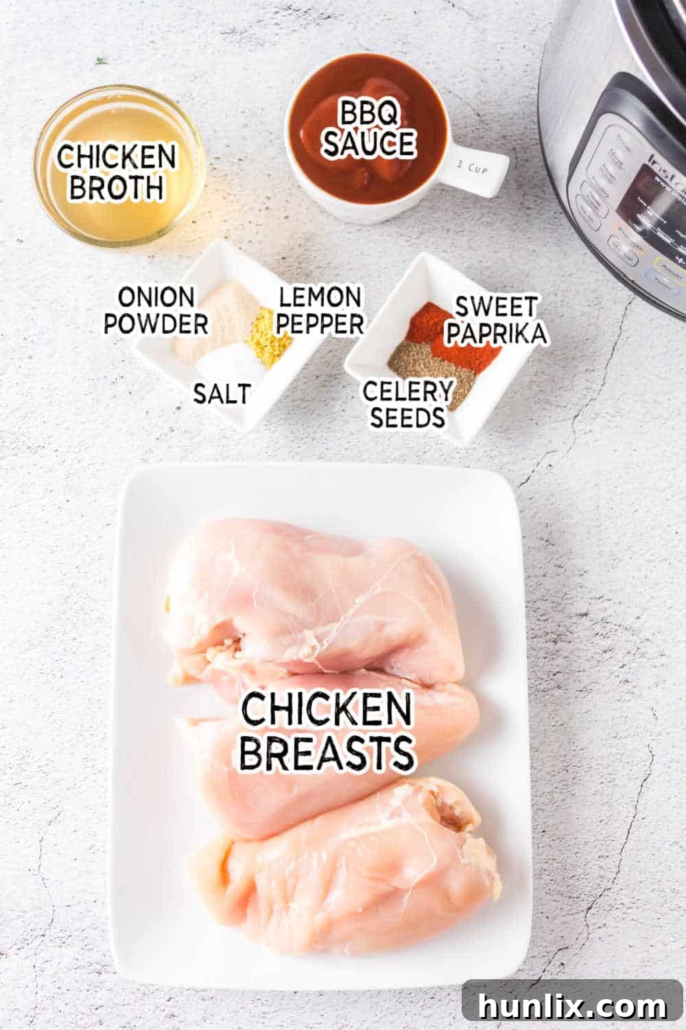 A selection of ingredients laid out, including chicken breasts, various spices, chicken broth, and a bottle of BBQ sauce.