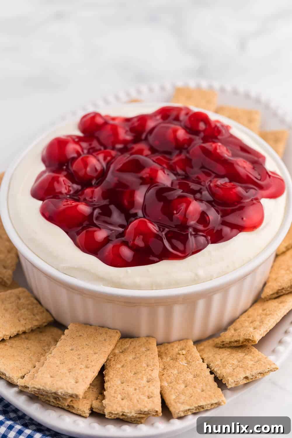 A generously portioned cherry cheesecake dip on a white serving platter, surrounded by crispy graham crackers, ready to be enjoyed as a delightful dessert or appetizer.