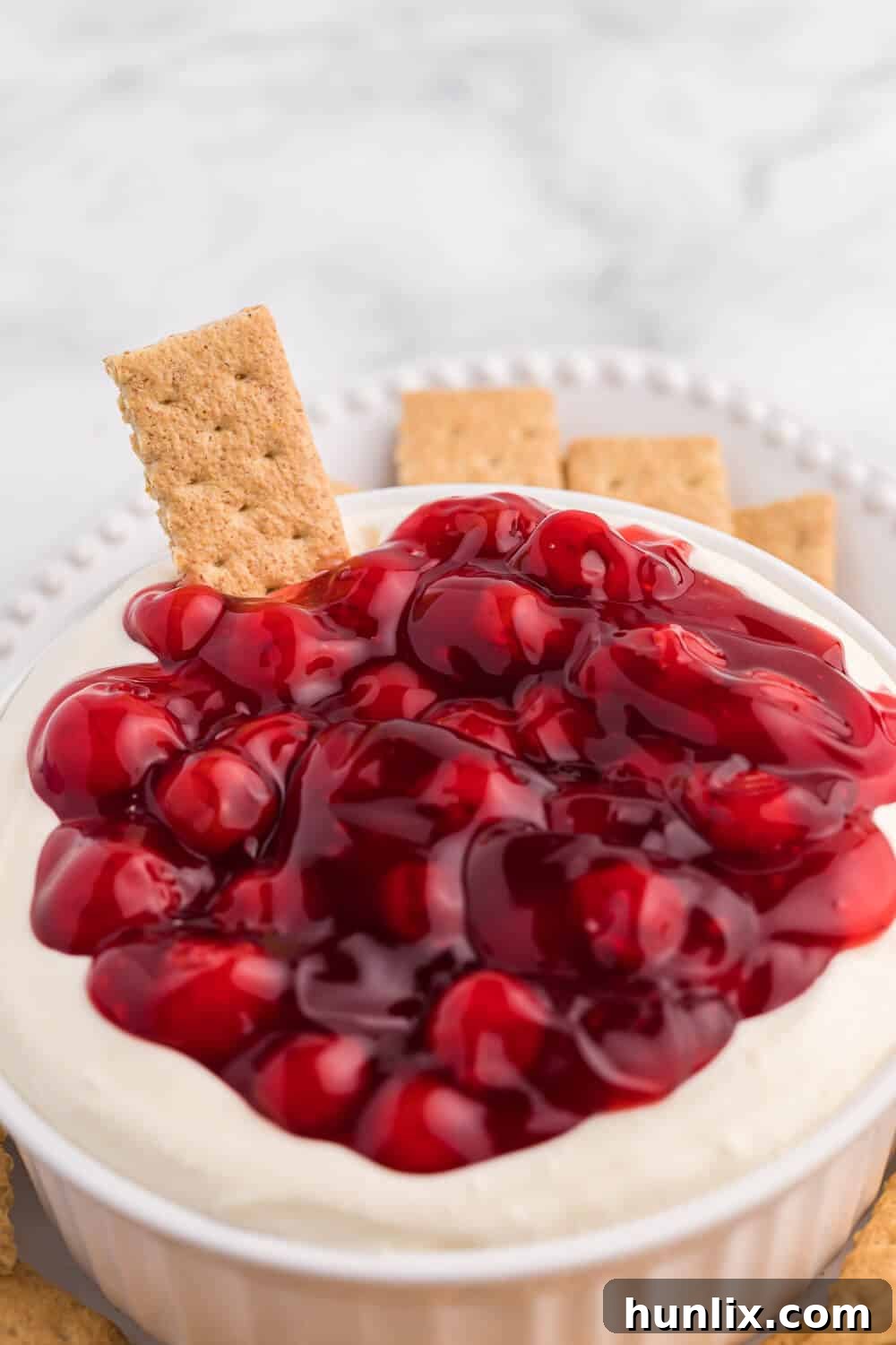 A close-up shot of a creamy cherry cheesecake dip, with a graham cracker perfectly dipped into its luscious texture, highlighting the rich cherry topping.