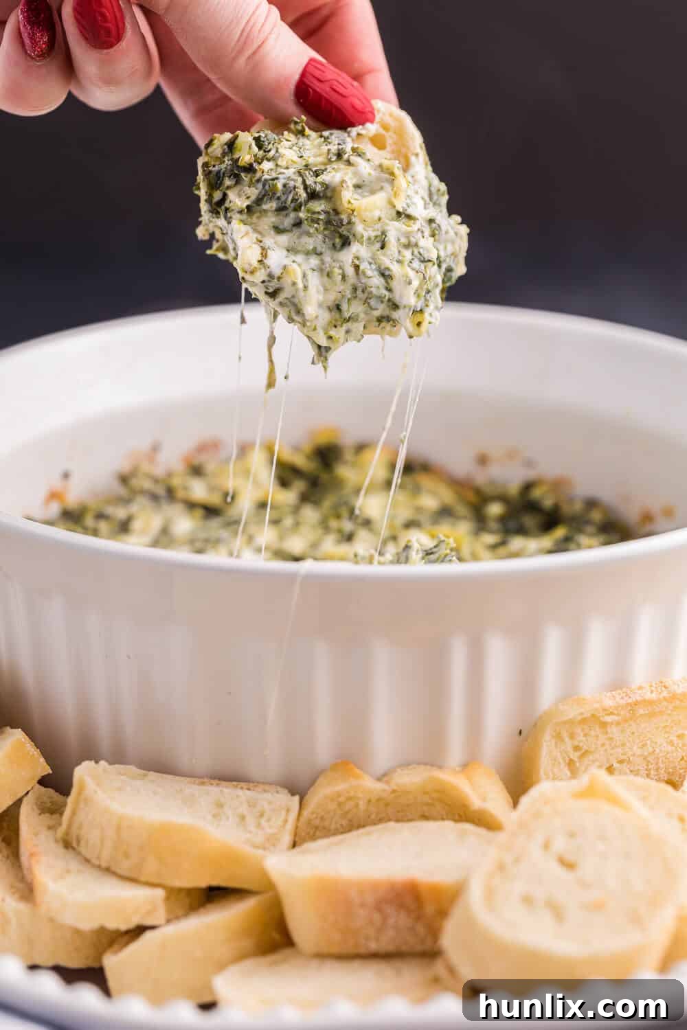 Creamy Artichoke Spinach Bliss 7 A hand holding a piece of baguette with spinach artichoke dip on it