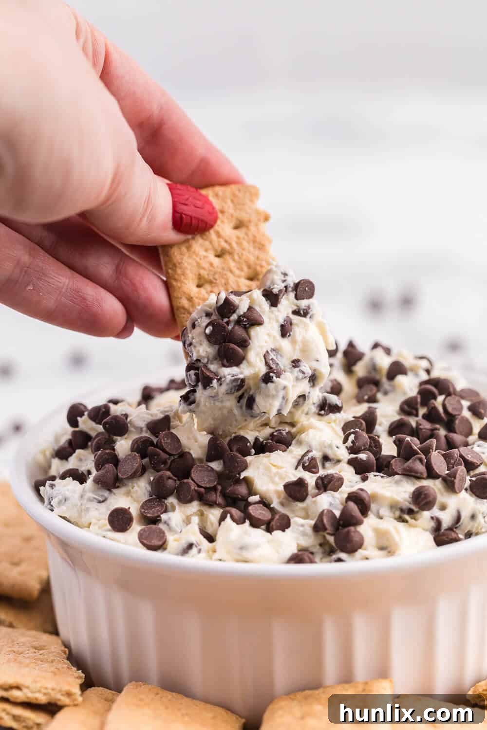 A hand dipping a graham cracker into a bowl of creamy Booty Dip.