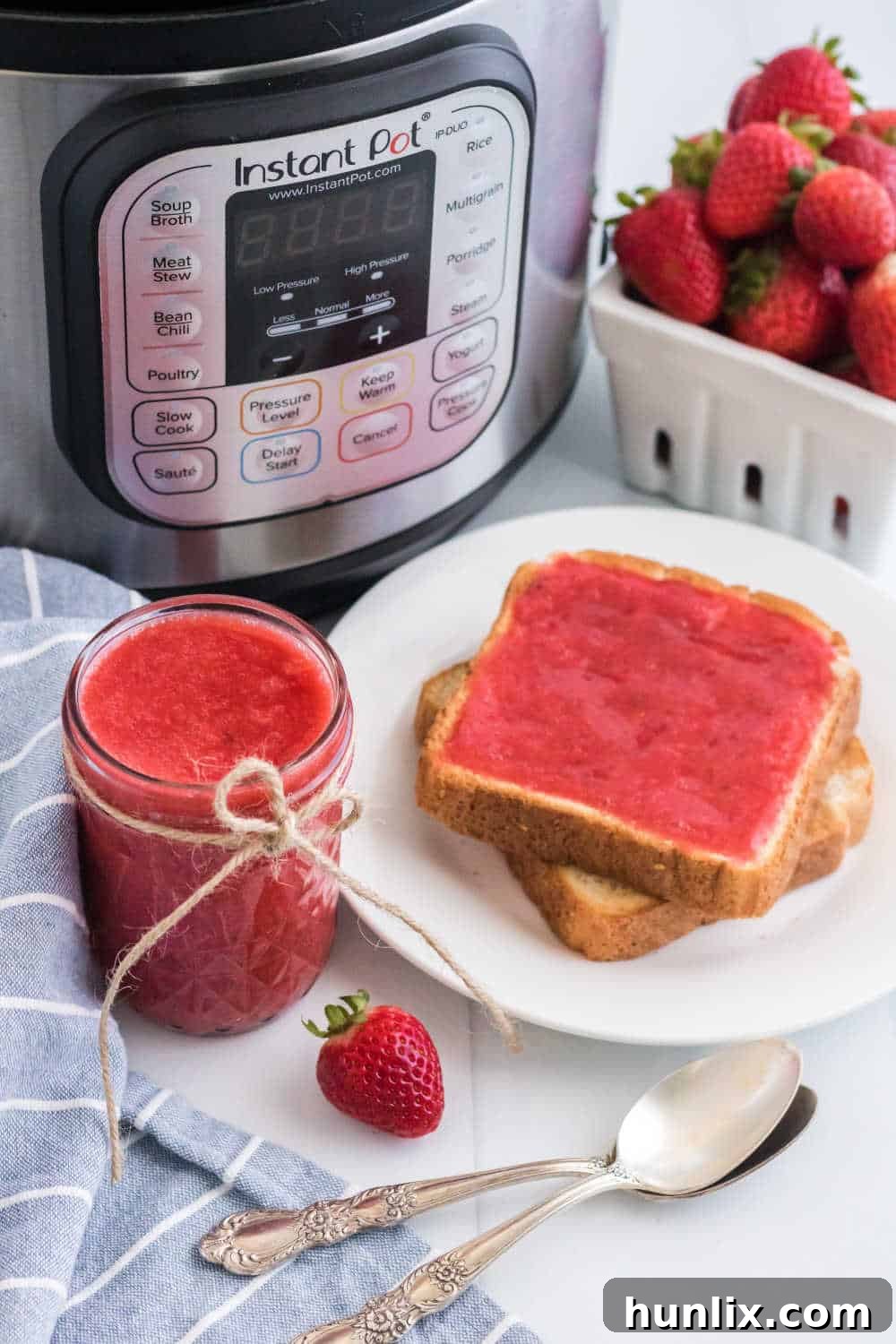 Effortless Instant Pot Strawberry Jam 9 A mason jar of Instant Pot Strawberry Jam sits next to a plate with two slices of toast, each generously spread with the homemade jam.