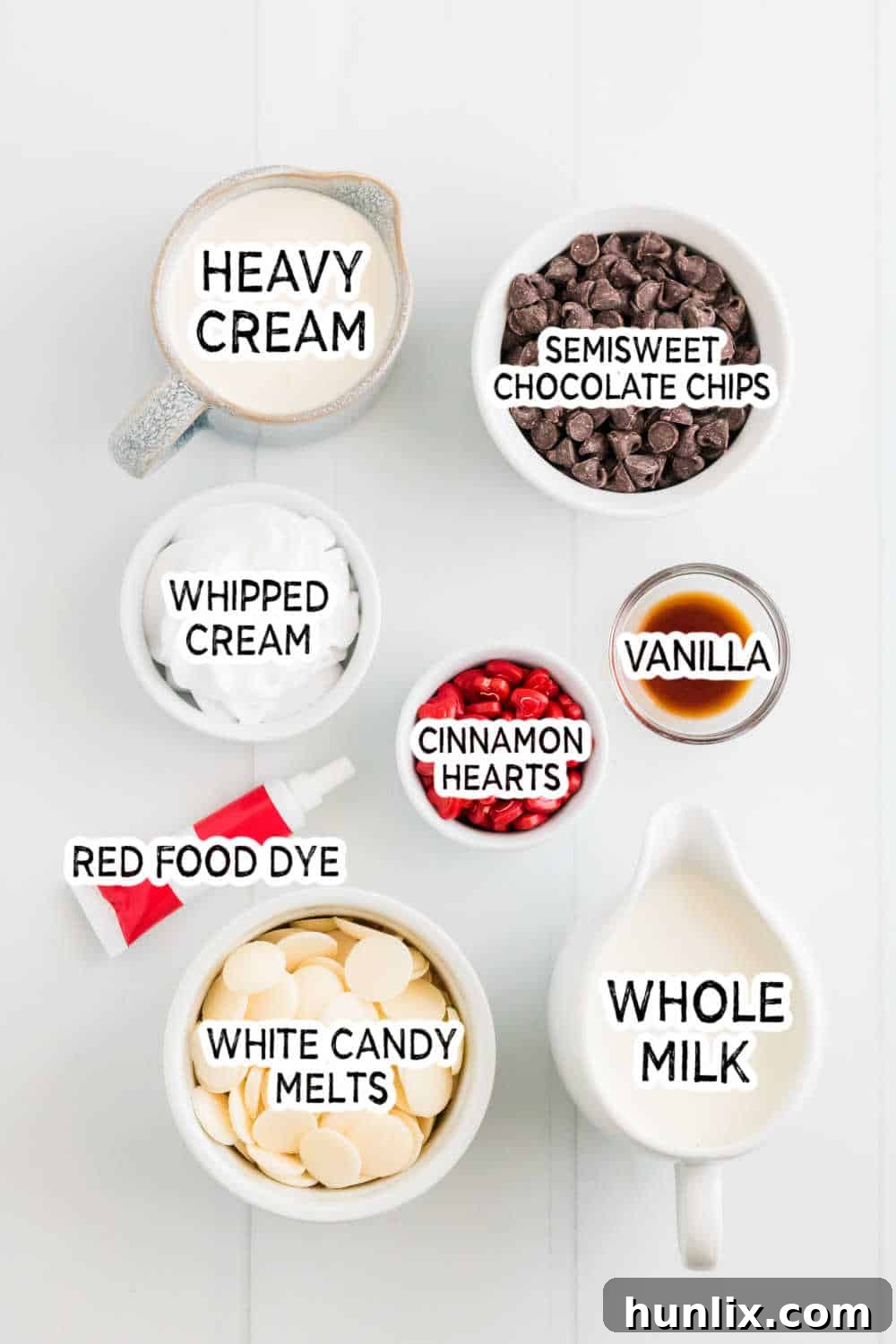 A selection of ingredients for red velvet hot chocolate, including milk, cream, chocolate chips, and red food dye, arranged on a white surface.