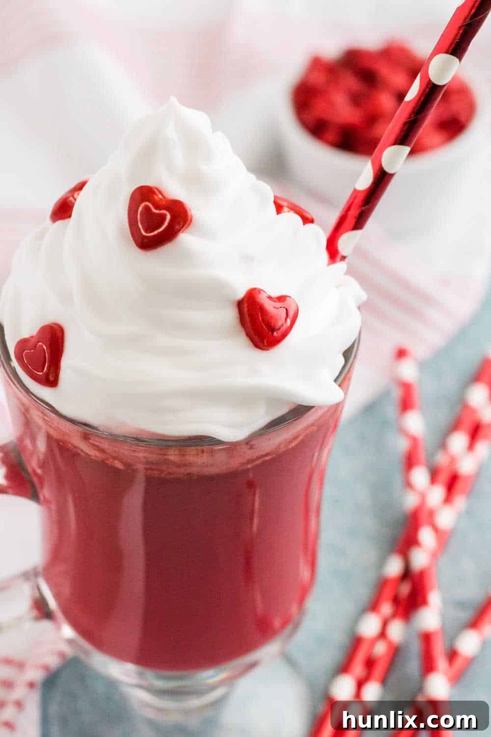 A single mug of red velvet hot chocolate, elegantly decorated for Valentine's Day with whipped cream, sprinkles, and a red bow.