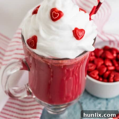 A mug of red velvet hot chocolate with a red straw, topped with whipped cream and sprinkles.