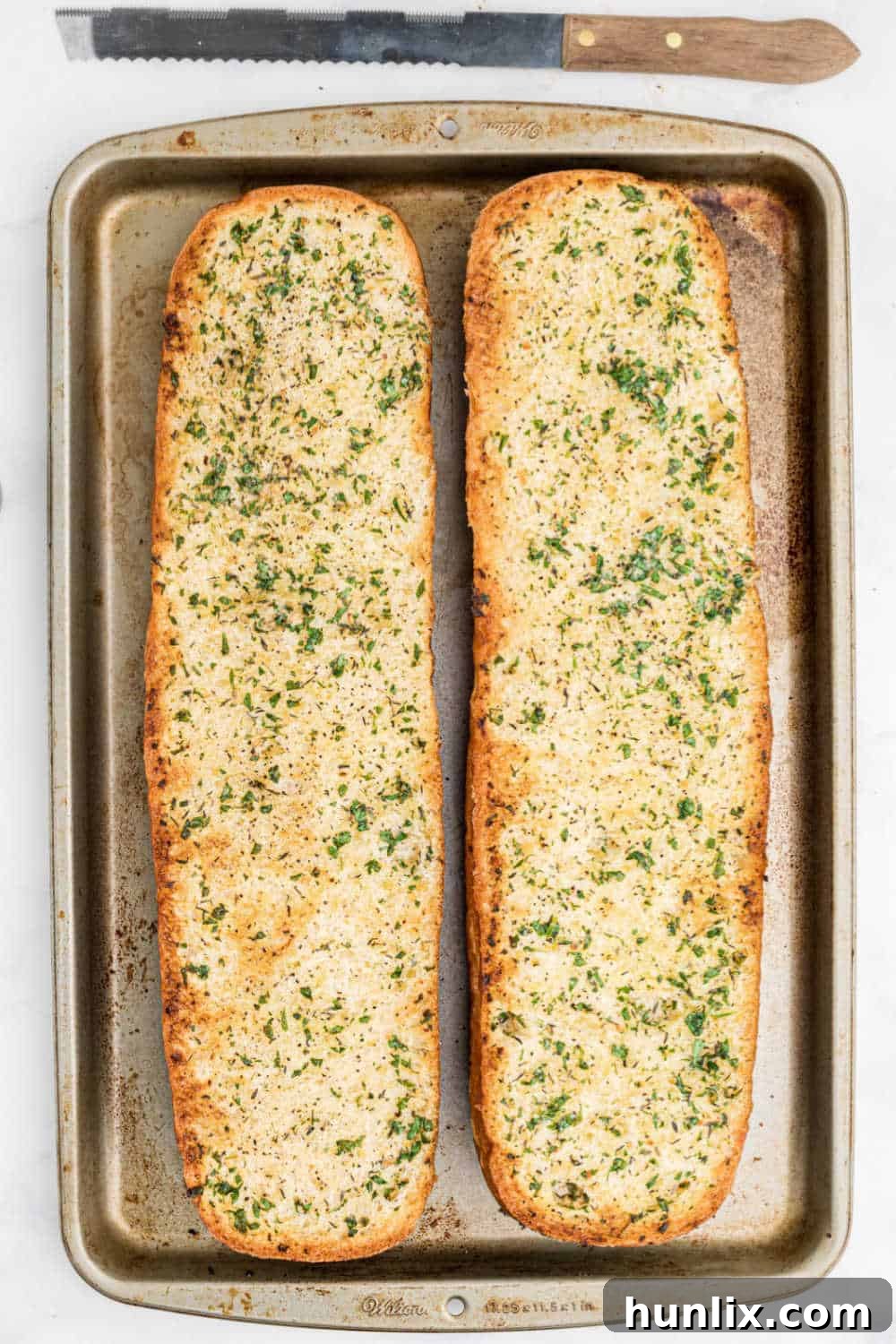 A perfectly golden-brown loaf of garlic bread, fresh from the oven, resting on a baking sheet.