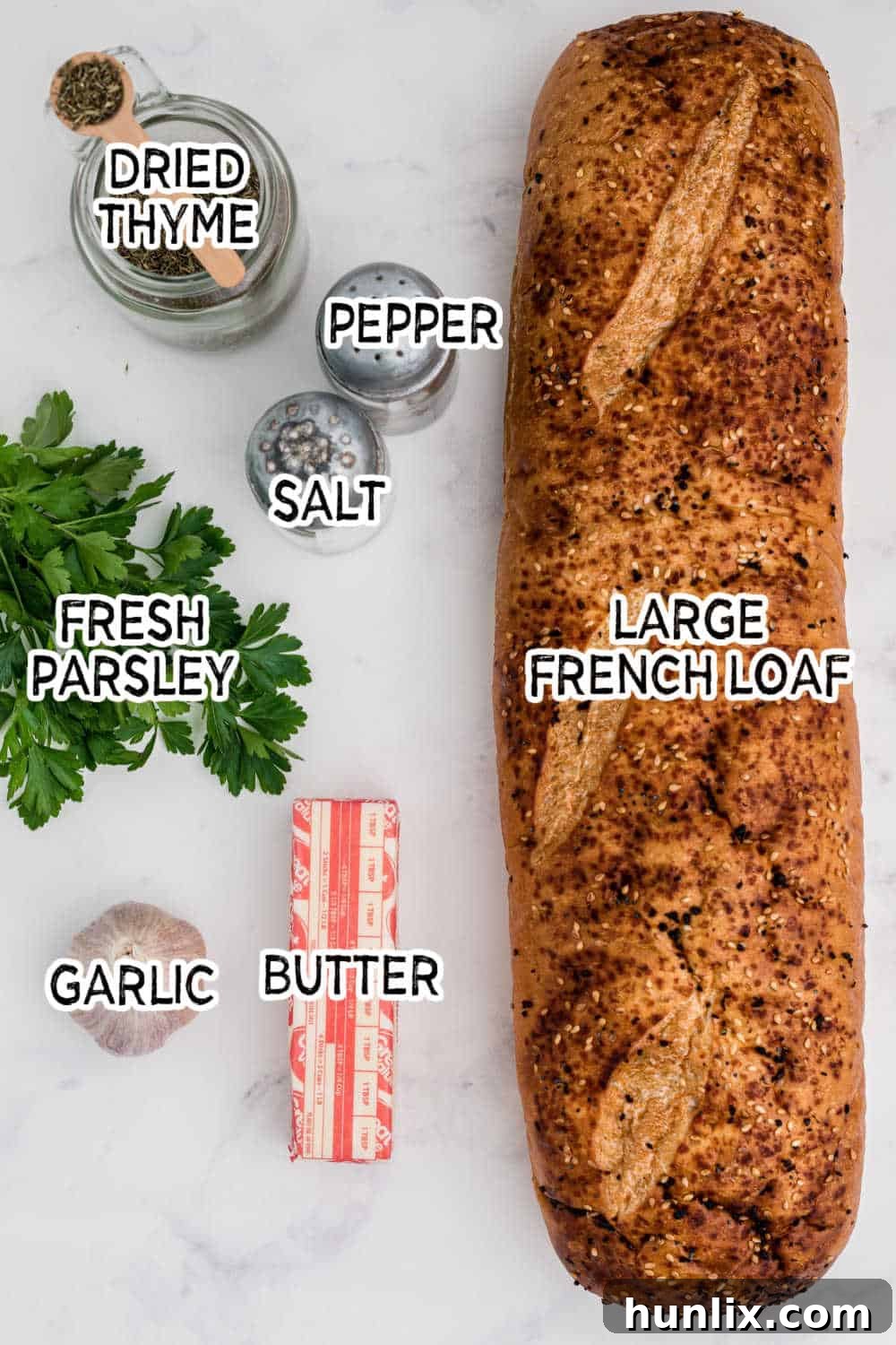 Fresh ingredients for garlic bread, including a French loaf, softened butter, garlic cloves, dried thyme, and fresh parsley.
