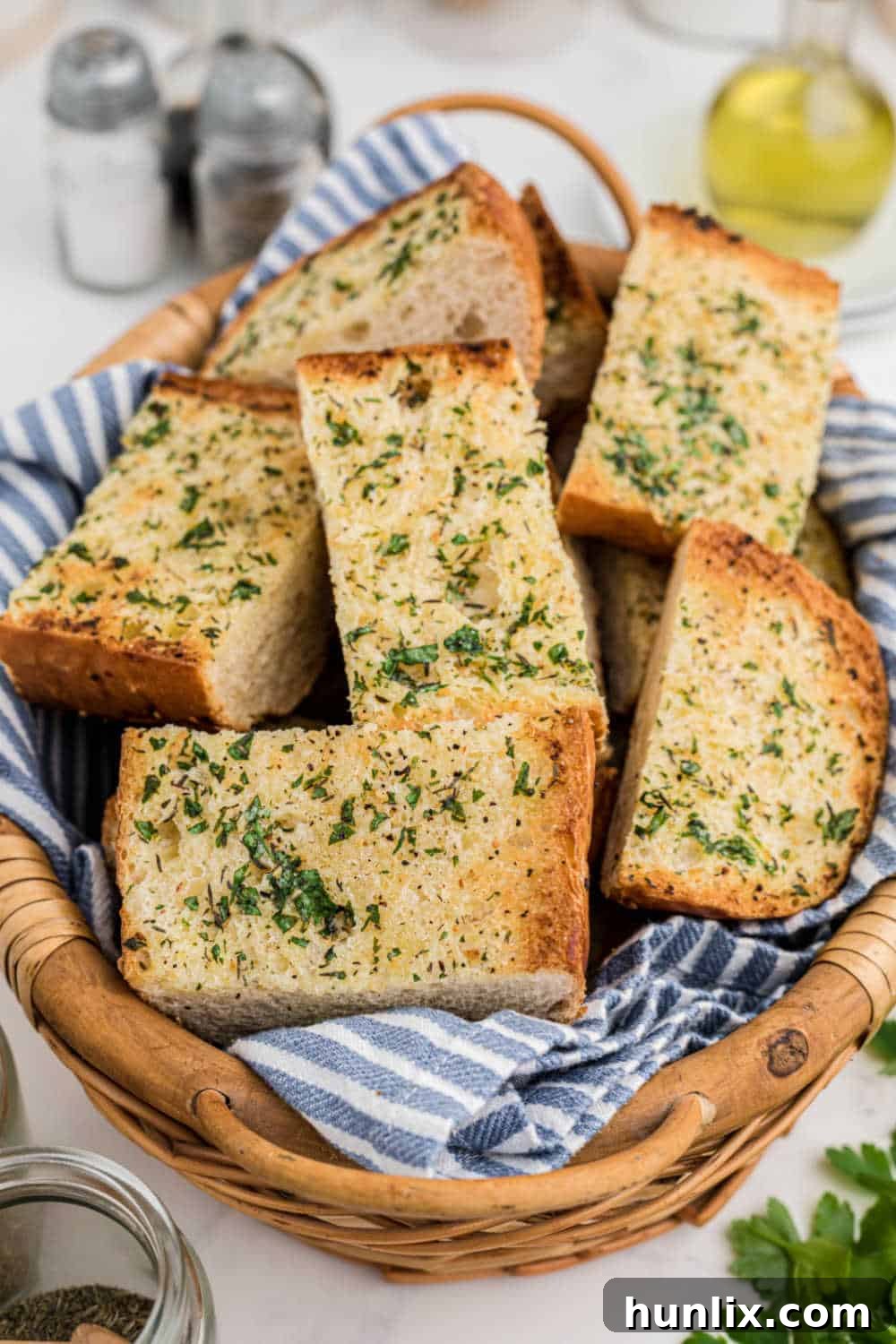 Numerous pieces of golden-brown garlic bread, some stacked, in a brown wicker basket.