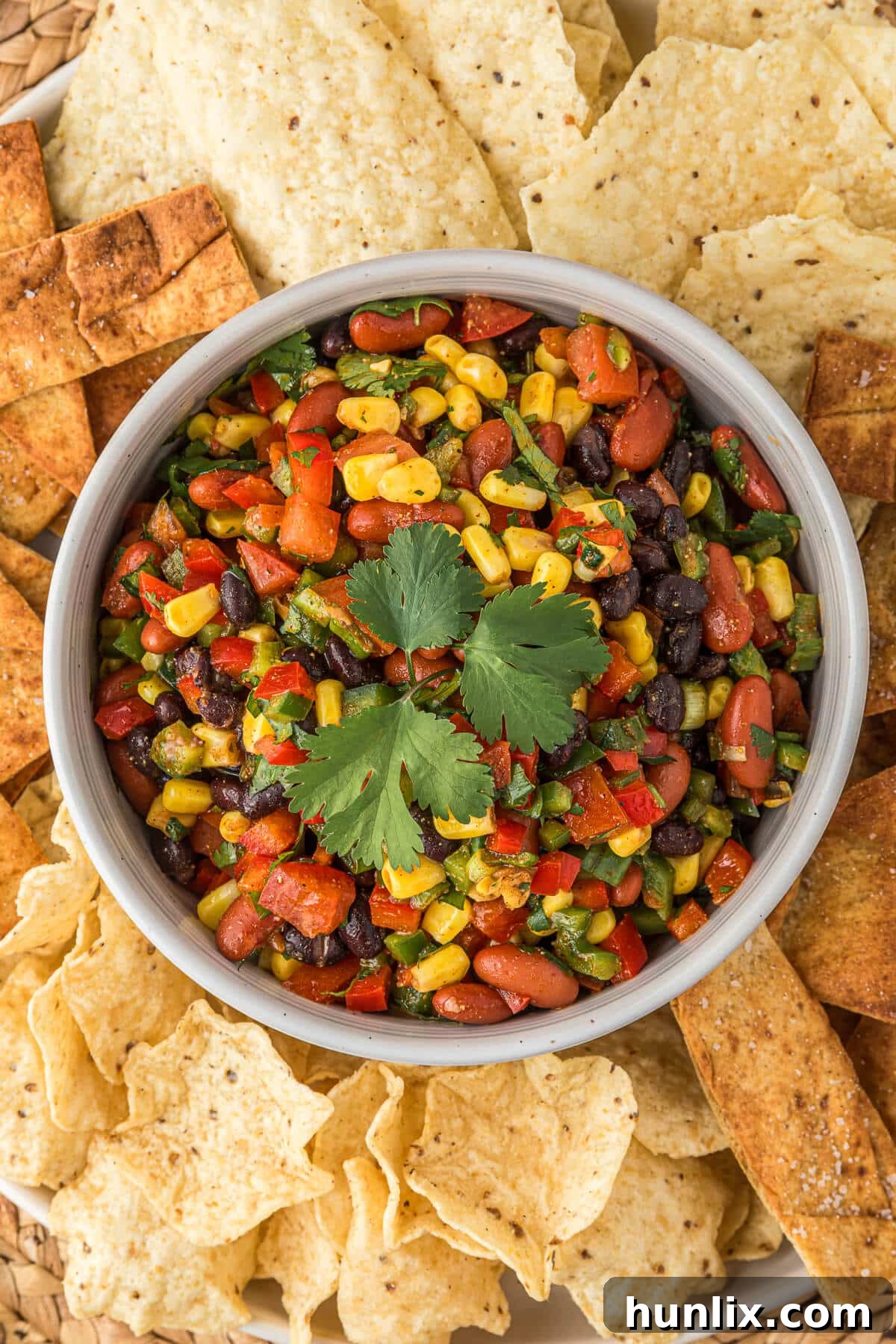 A bowl of Cowboy Caviar garnished with fresh cilantro, surrounded by crisp tortilla chips on a wooden table.