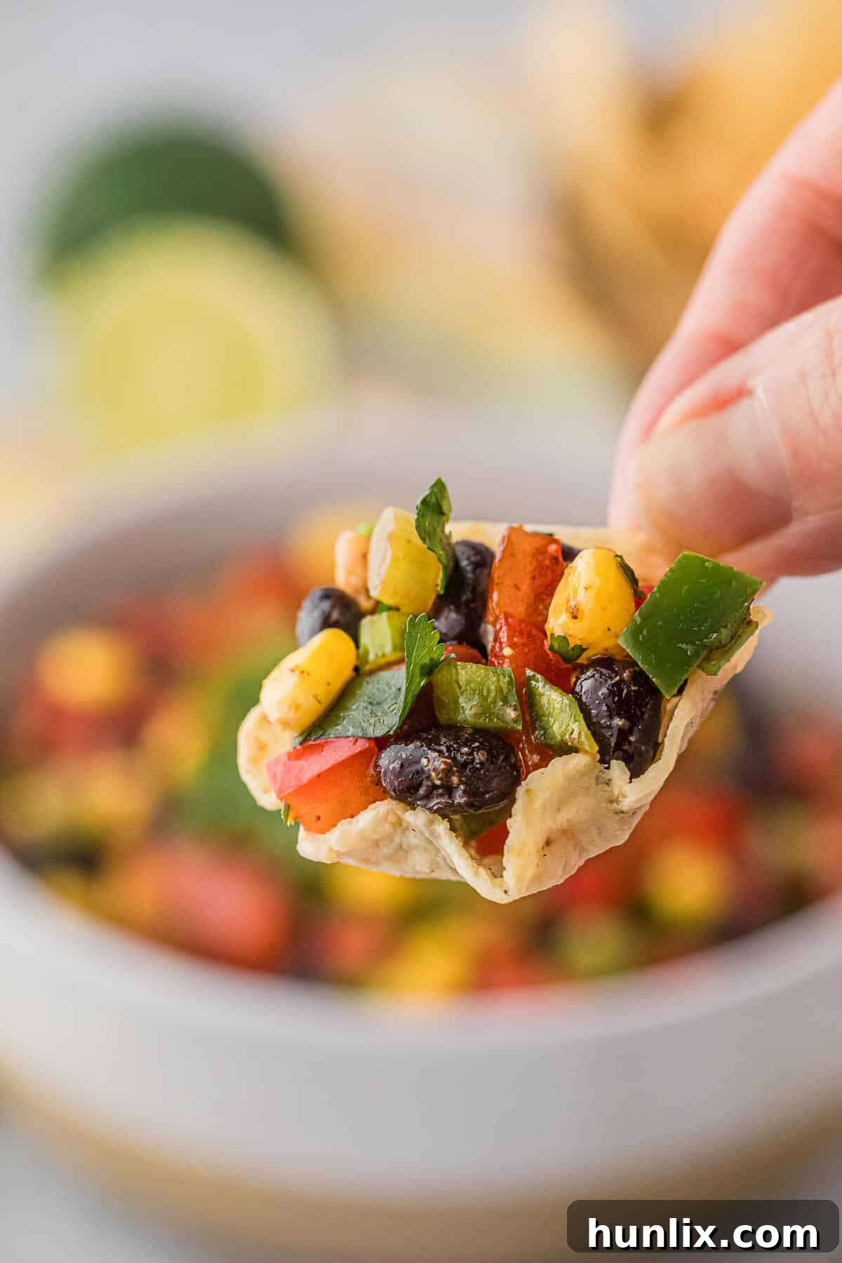 A hand holding a tortilla chip topped with a spoonful of Cowboy Caviar.
