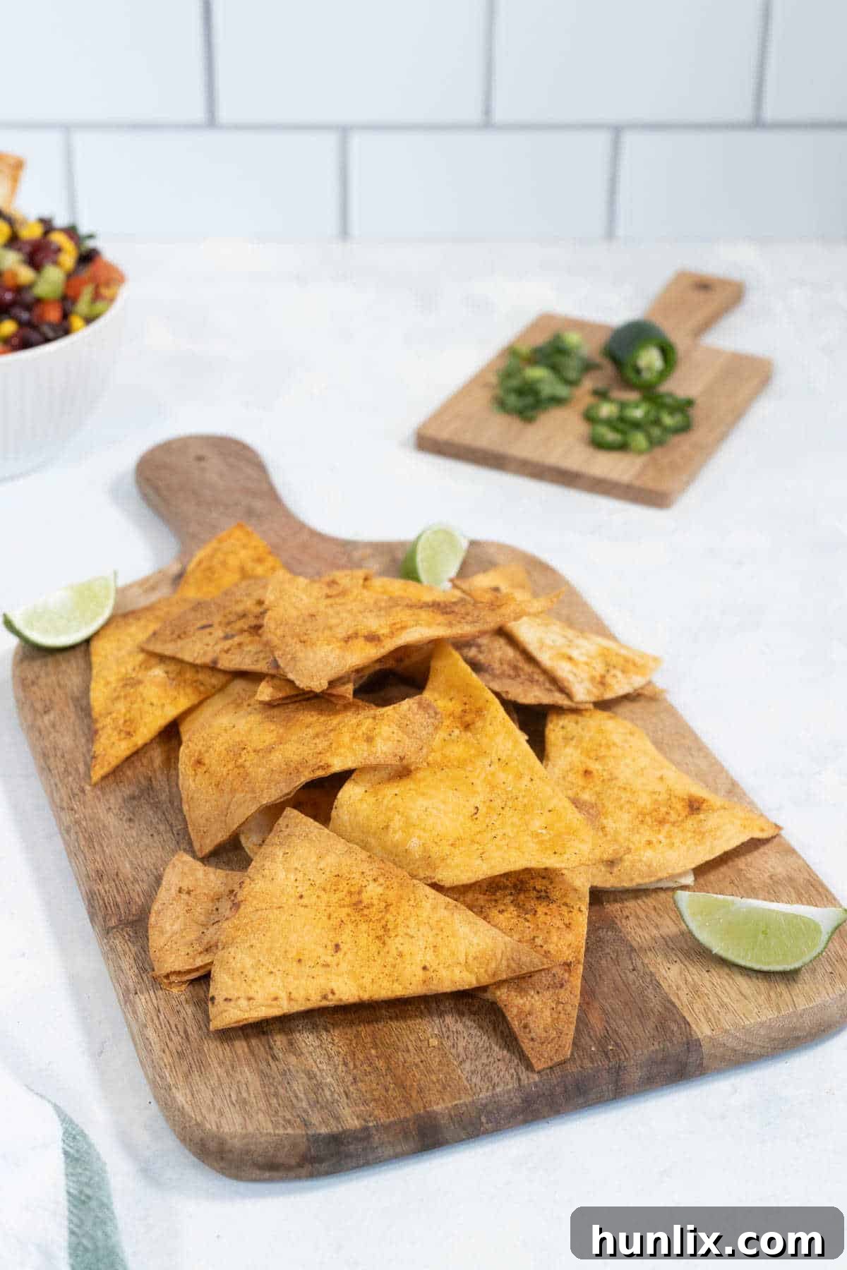 Air fryer tortilla chips on a wooden cutting board, garnished with cilantro and lime wedges.