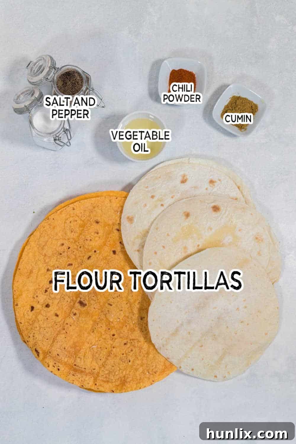 A flat lay of ingredients for air fryer tortilla chips: flour tortillas, a bottle of vegetable oil, a small bowl of chili powder, a small bowl of cumin, and a salt and pepper grinder.