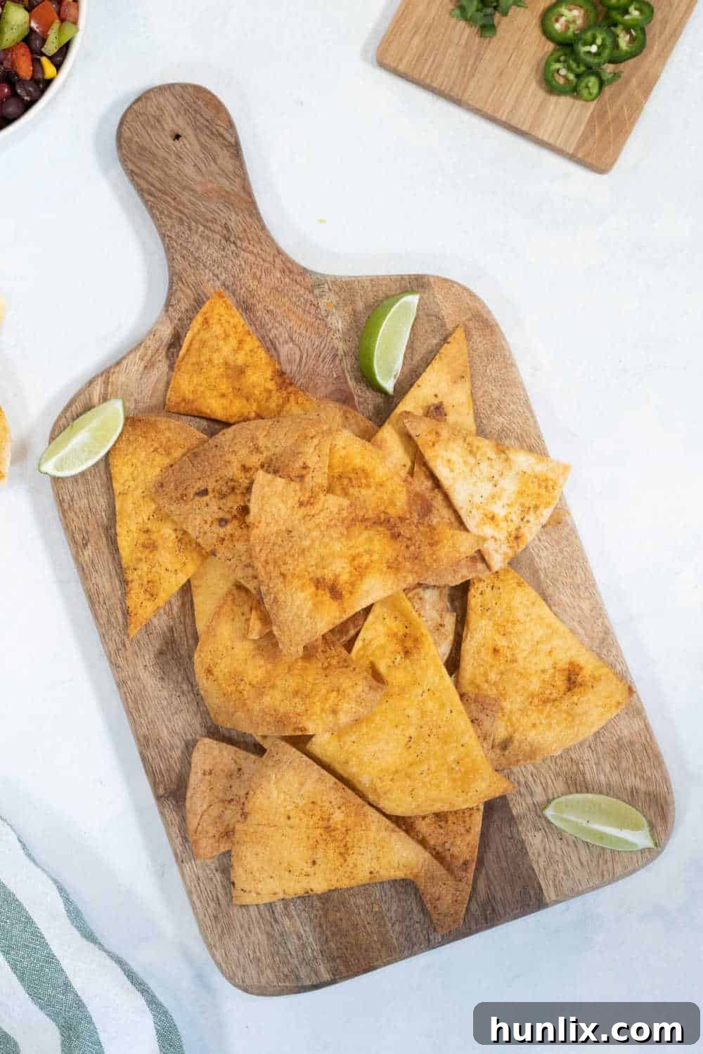 Air fryer tortilla chips on a wooden cutting board with sliced limes, creating a fresh and inviting presentation.