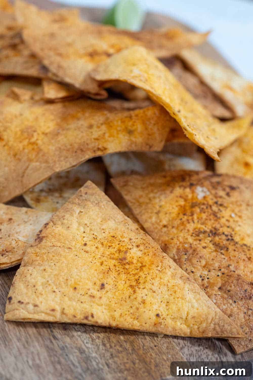 A large pile of golden-brown air fryer tortilla chips on a wooden board, ready for serving.