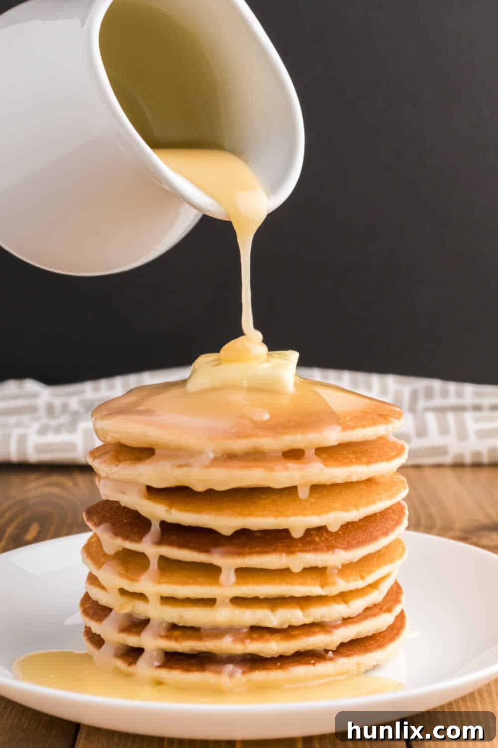 Golden Pancake Drizzle 7 A pitcher drizzling syrup over a stack of pancakes.