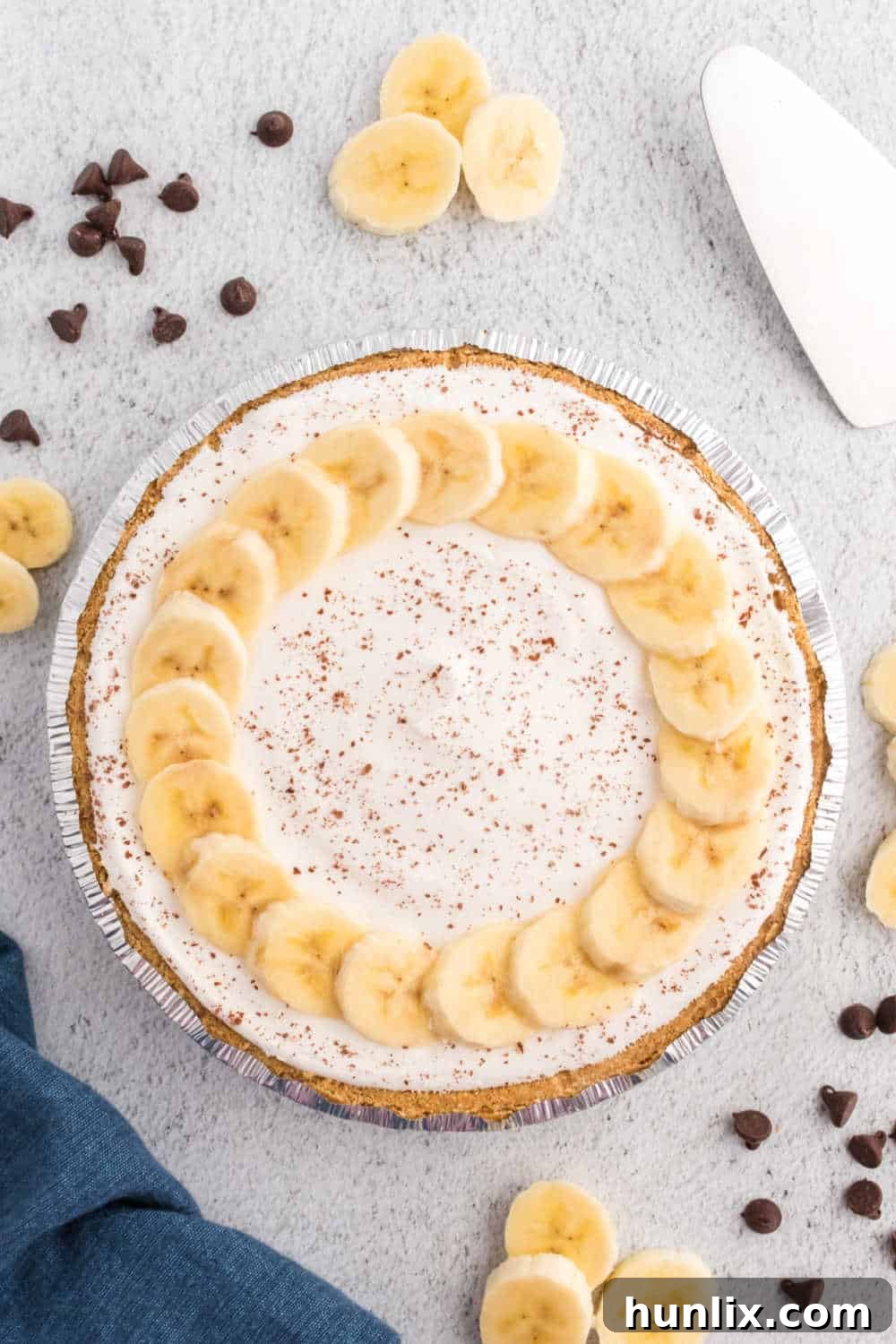 Black bottom banana cream pie on grey surface. A generous slice is visible, showcasing the distinct layers of chocolate, banana, and cream.