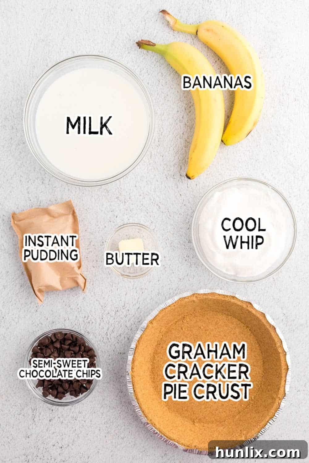 Ingredients for Black Bottom Banana Cream Pie laid out on a white surface, including chocolate chips, milk, butter, bananas, pudding mix, and Cool Whip.