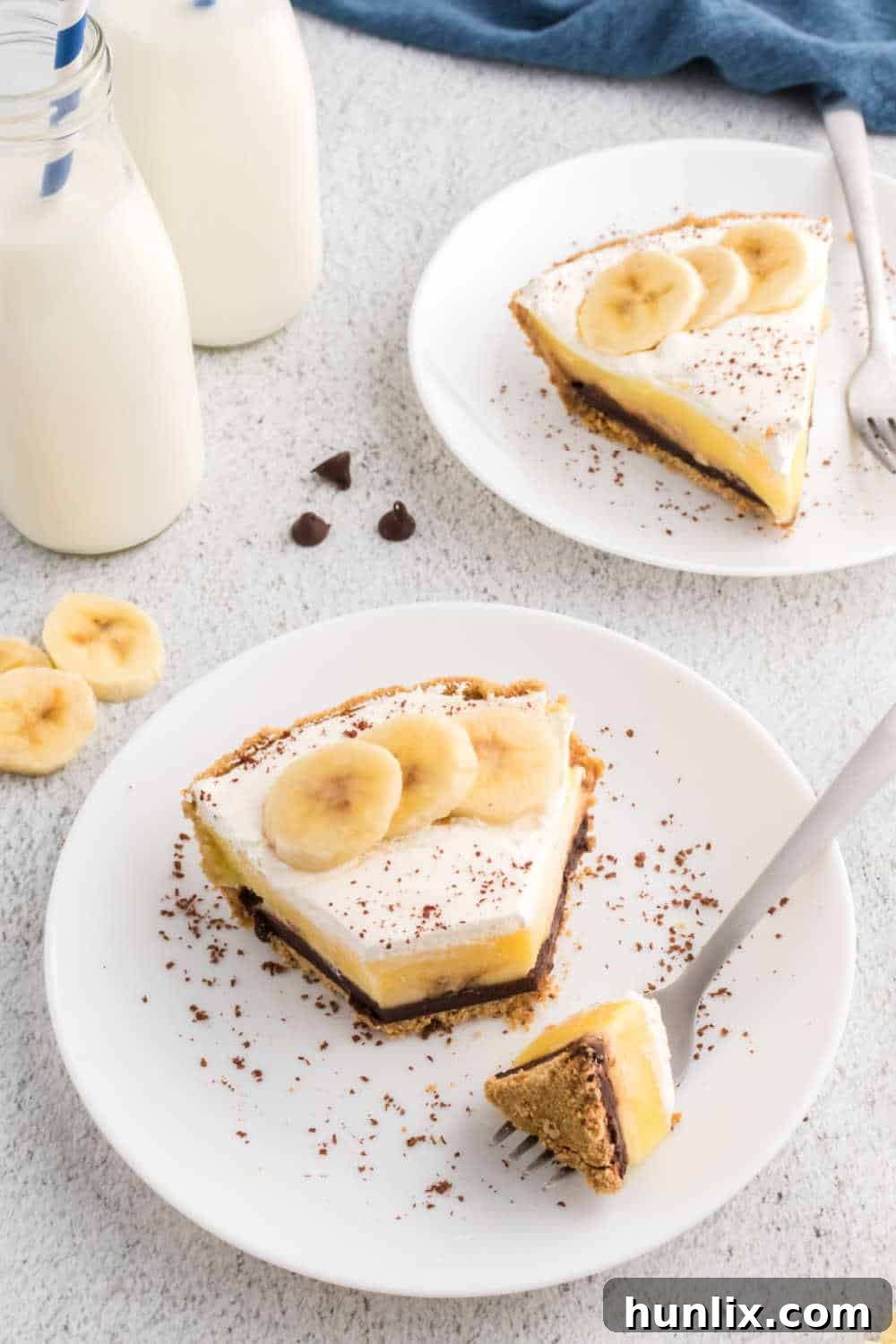 A slice of black bottom banana cream pie on a white plate with a fork taking a bite, showing all the layers clearly.