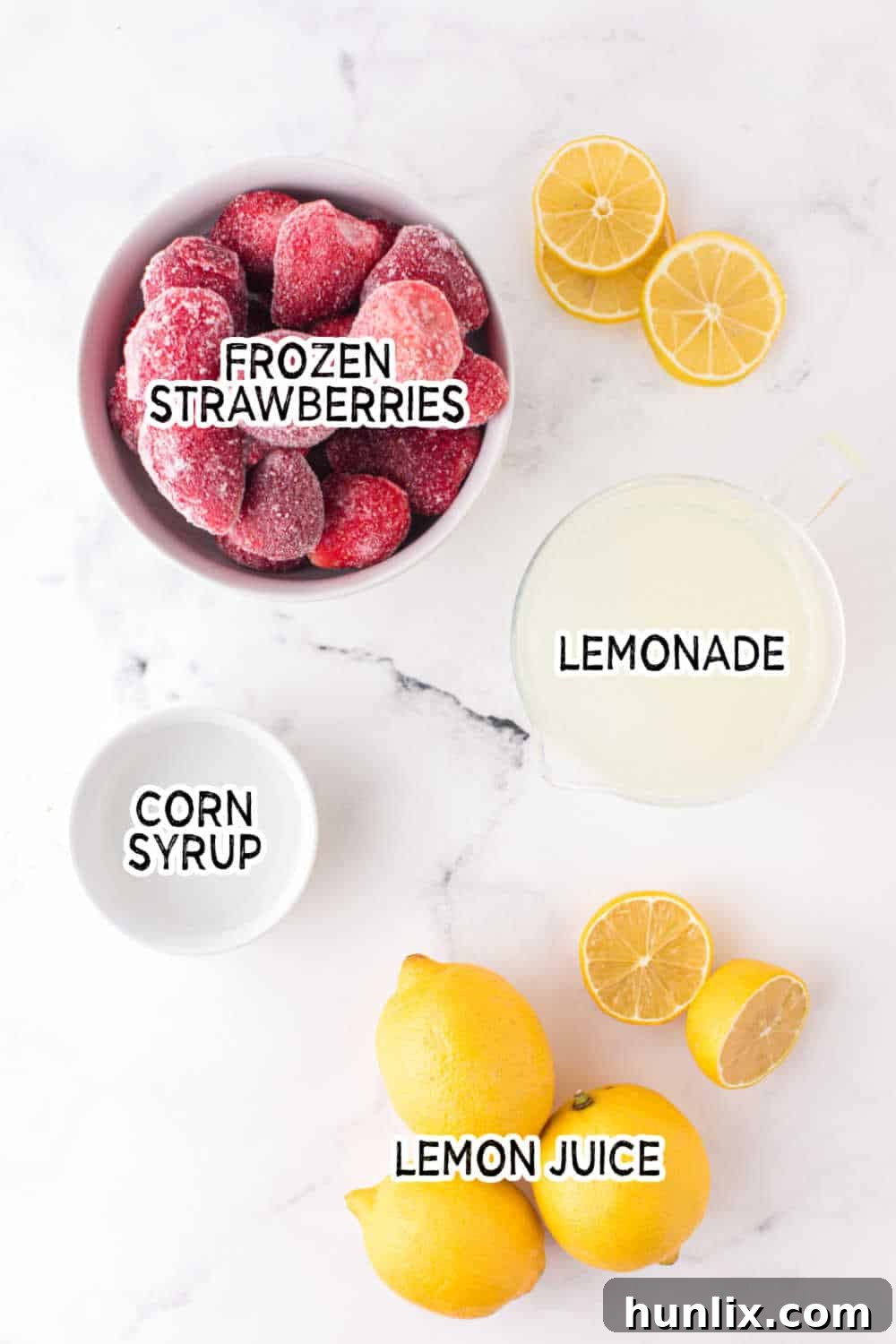 A flat lay photograph showcasing the four key ingredients: a bag of frozen strawberries, a pitcher of lemonade, a bowl of lemon juice, and a bottle of corn syrup.