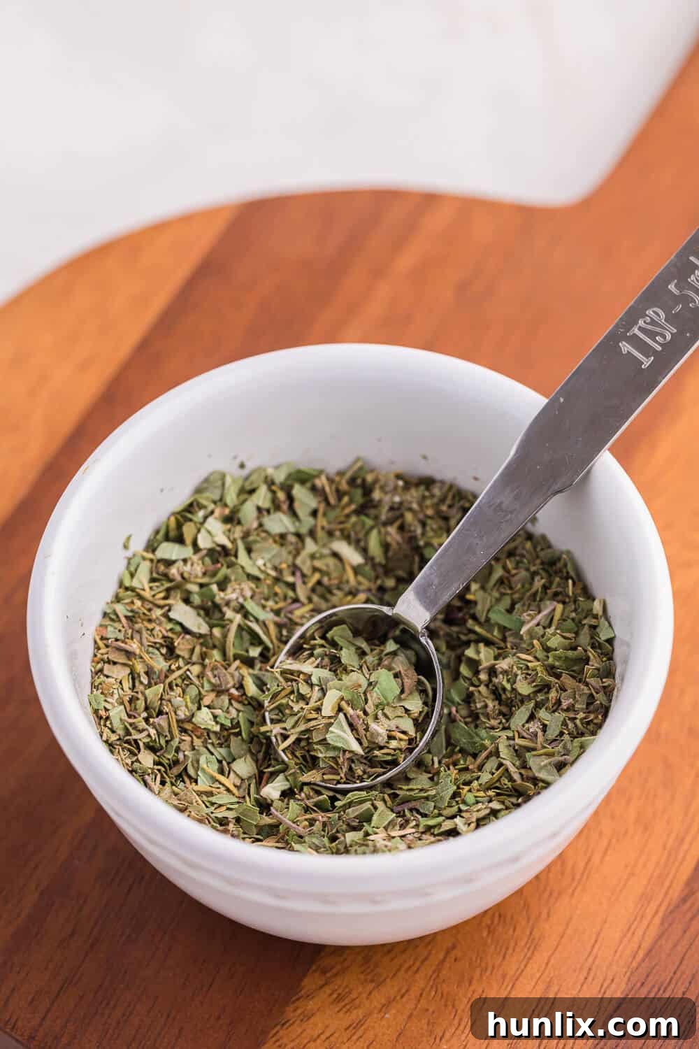 Homemade Italian seasoning in a small bowl with a measuring spoon, ready for use.
