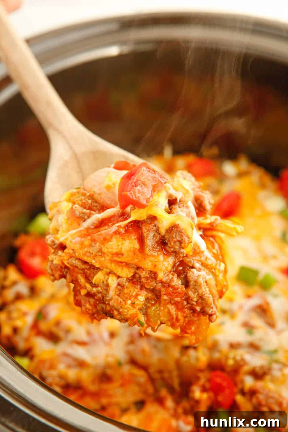 Fall-Apart Beef Enchilada Slow Cooker Supper 7 A serving spoon scoops a generous portion of cheesy slow cooker beef enchilada casserole from the crockpot, showcasing the layers of meat, tortillas, and melted cheese, ready for plating.