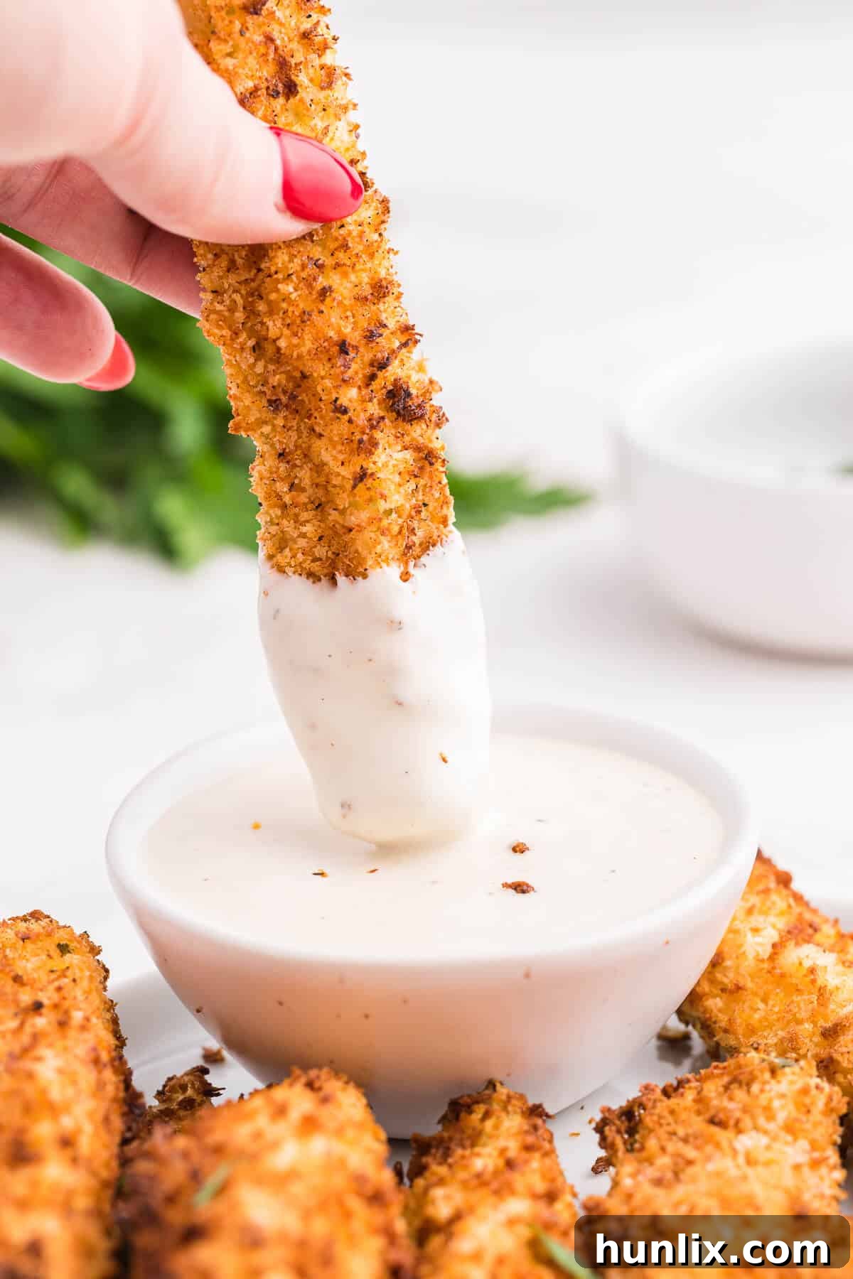 A hand enthusiastically dipping a golden-brown air fryer fried pickle spear into a creamy ranch dressing, emphasizing its deliciousness and the perfect pairing.