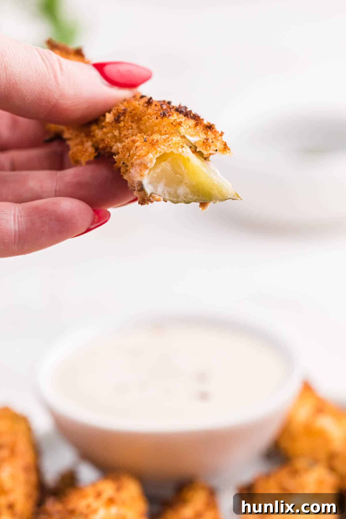 A close-up of a perfectly air-fried pickle spear, bitten in half to reveal the tender dill pickle inside its golden, crispy breading.