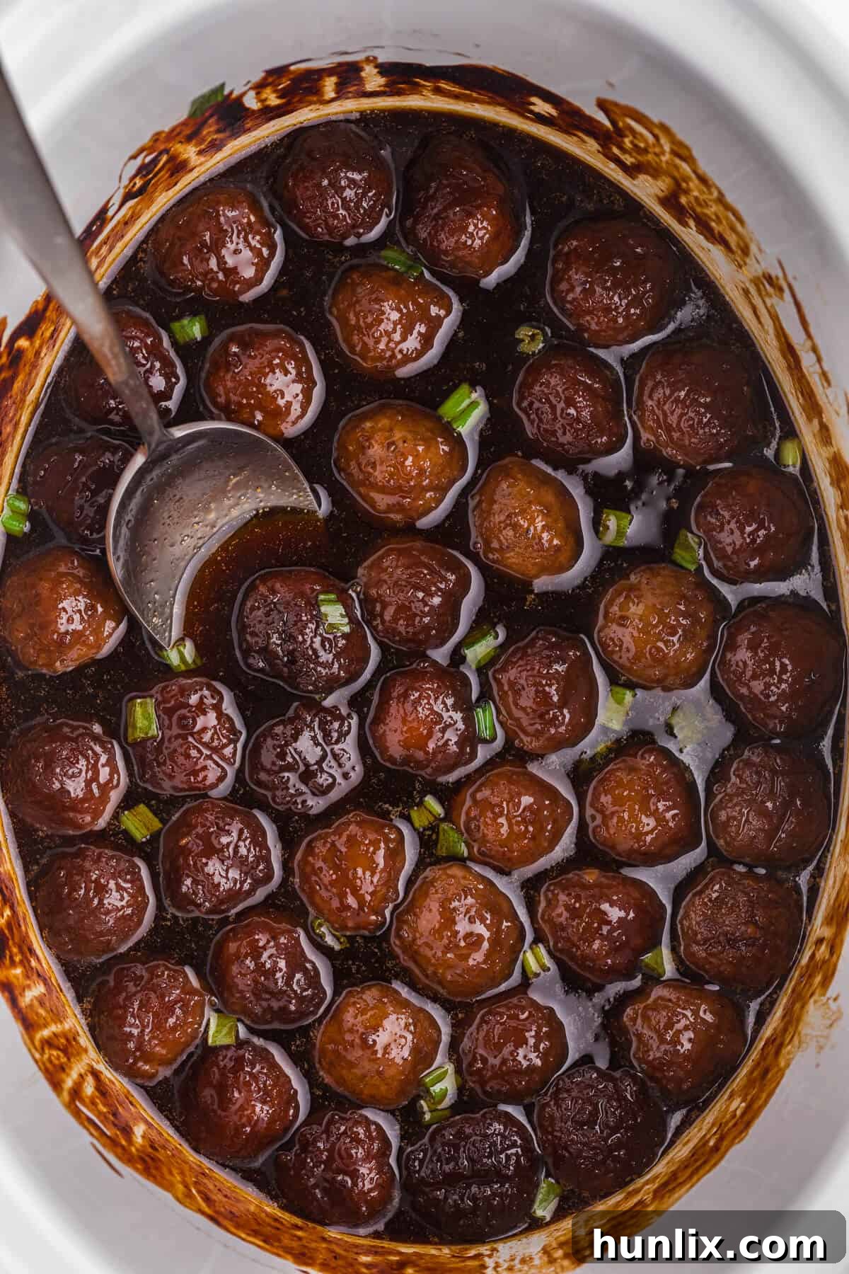 Grape-Glazed Meatballs 6 Grape jelly meatballs in a crockpot with a serving spoon.