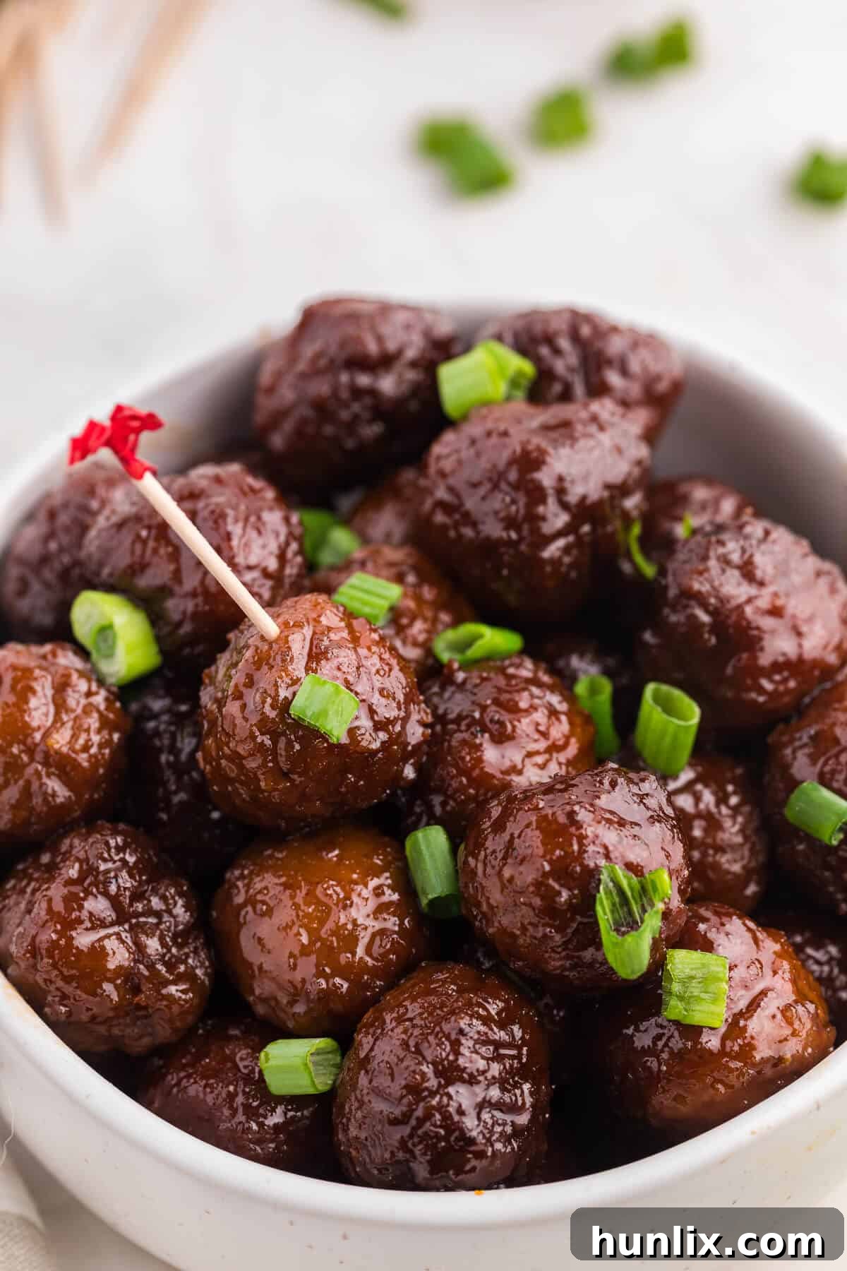 Grape-Glazed Meatballs 8 Grape jelly meatballs in a bowl with a toothpick in one meatball.