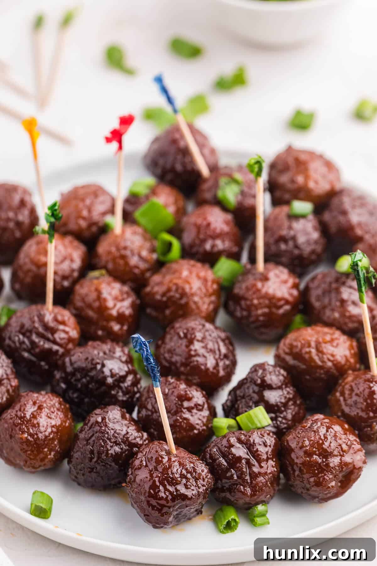 Grape-Glazed Meatballs 9 Grape jelly meatballs on a plate with toothpicks in some meatballs.
