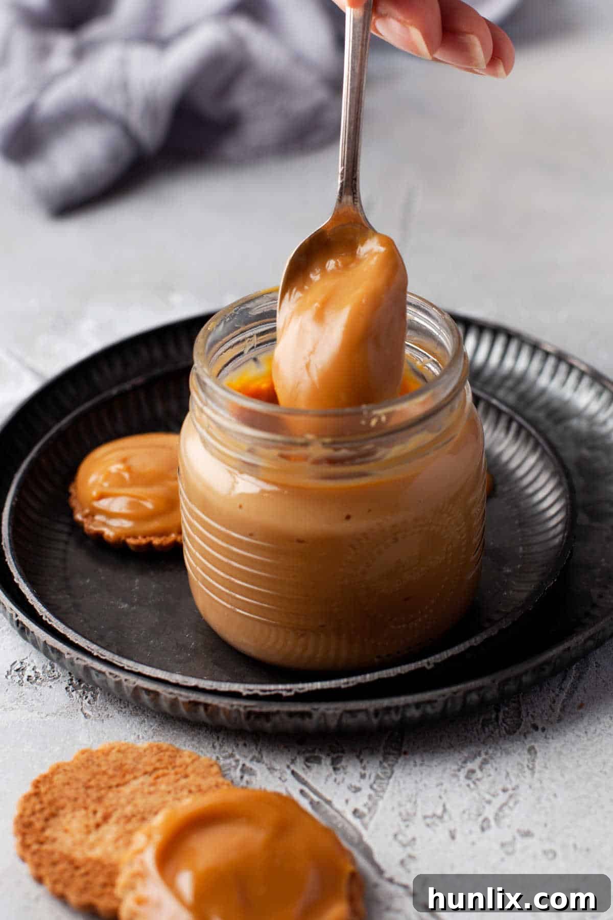A spoon emerges from a glass jar filled with golden, creamy Instant Pot Dulce de Leche, highlighting its rich texture and inviting color.