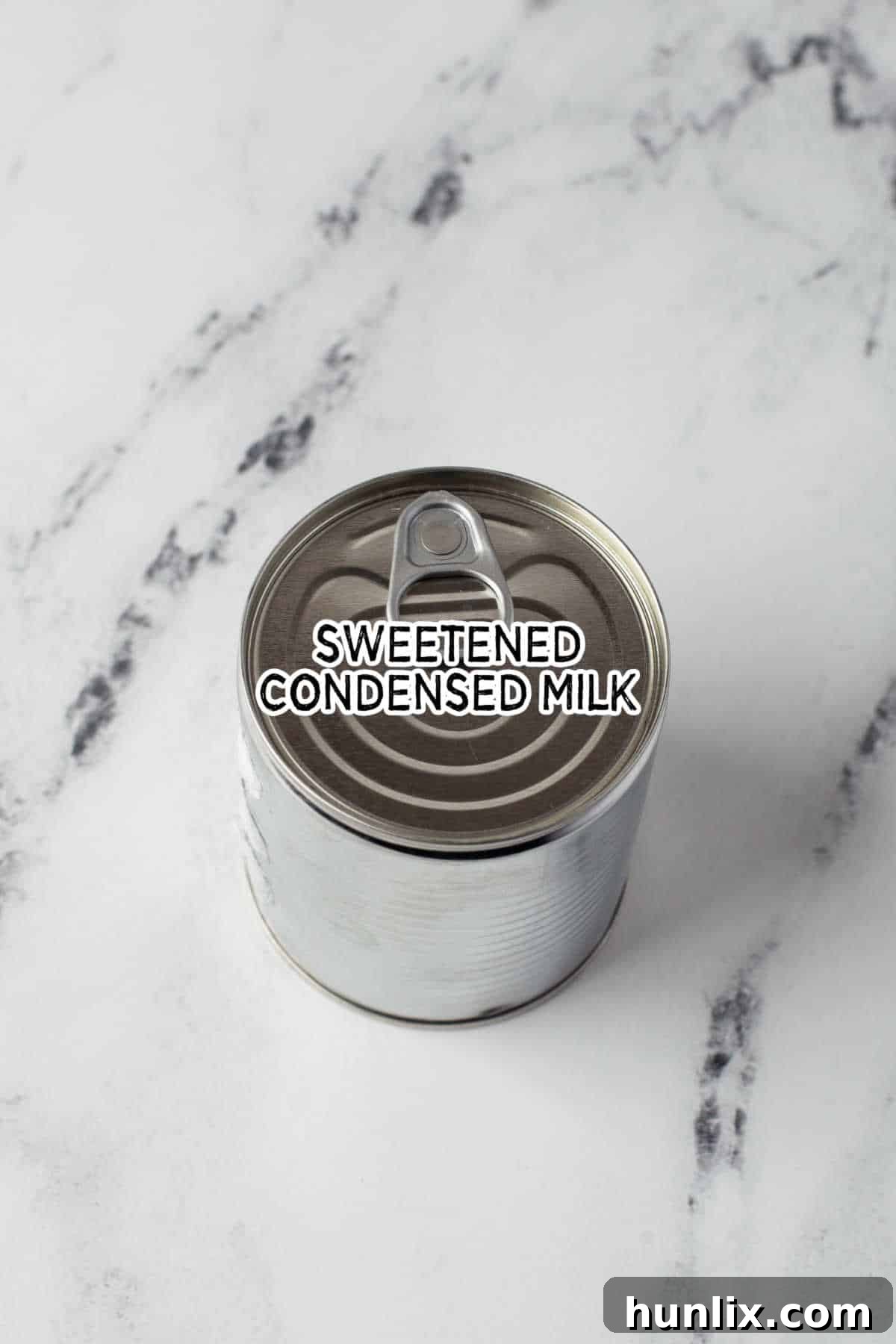A single can of sweetened condensed milk, the sole ingredient for making homemade dulce de leche, rests on a rustic wooden surface.