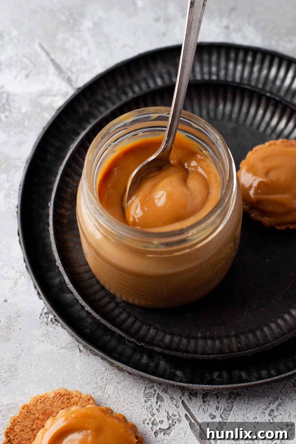 A close-up shot of a glass jar filled with rich, golden dulce de leche, with a spoon resting inside, inviting a taste.